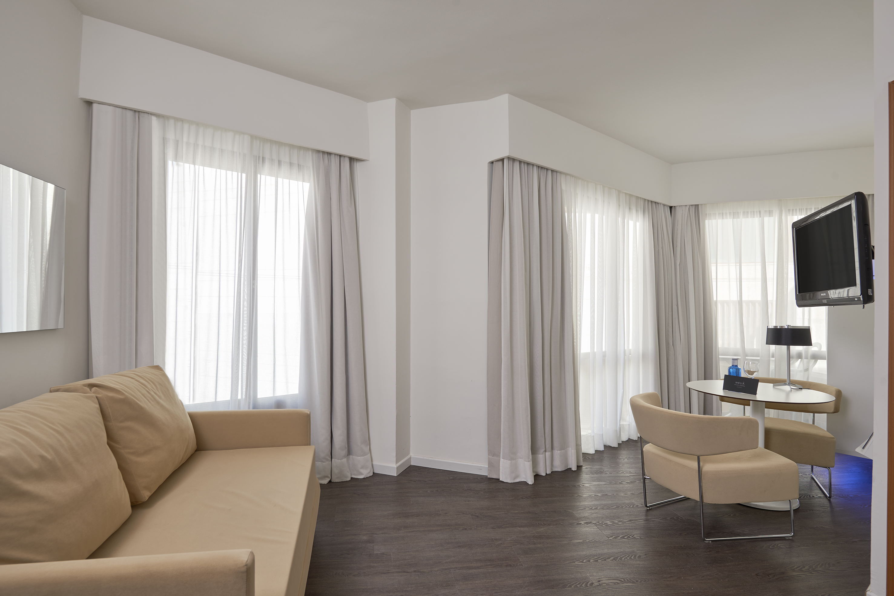 Modern hotel suite living area with sofa, dining table, and TV.
