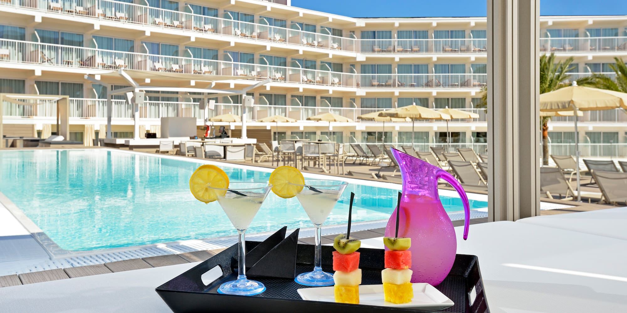 a tray of fruit and a drink on a table by a pool