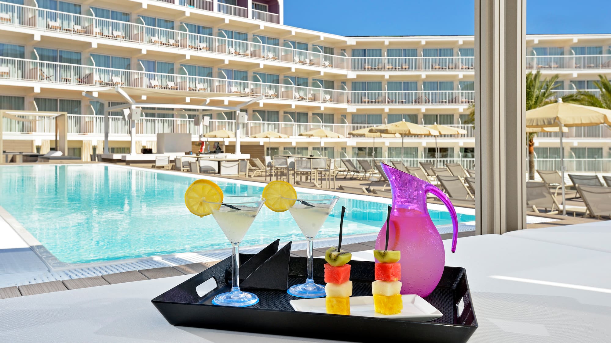 a tray of fruit and a drink on a table by a pool