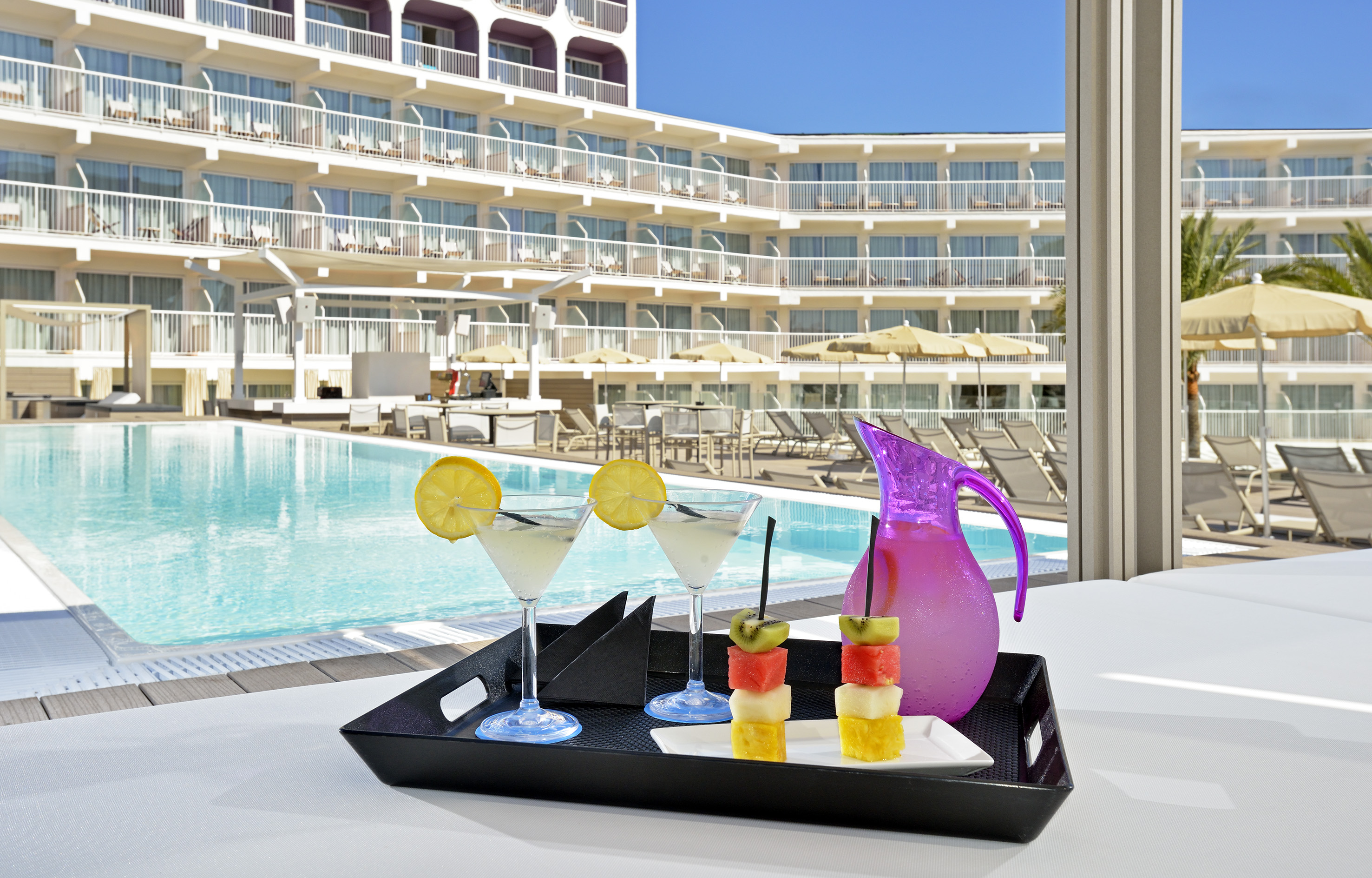 a tray of fruit and a drink on a table by a pool