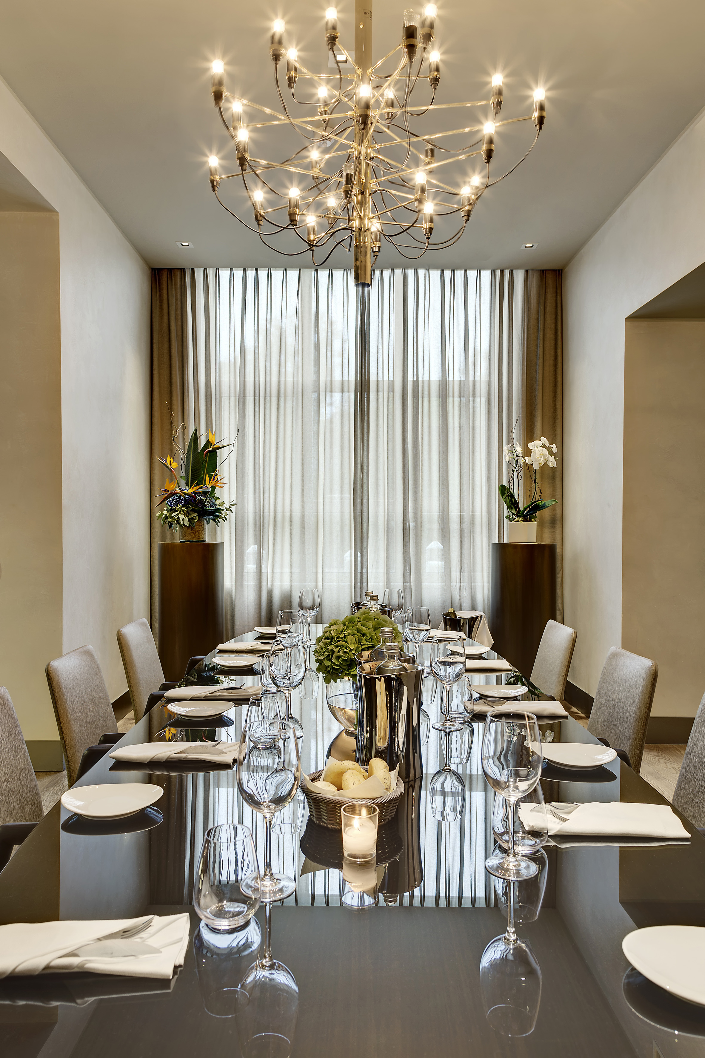 Elegant dining room with long set table, modern chandelier, and chic decor.