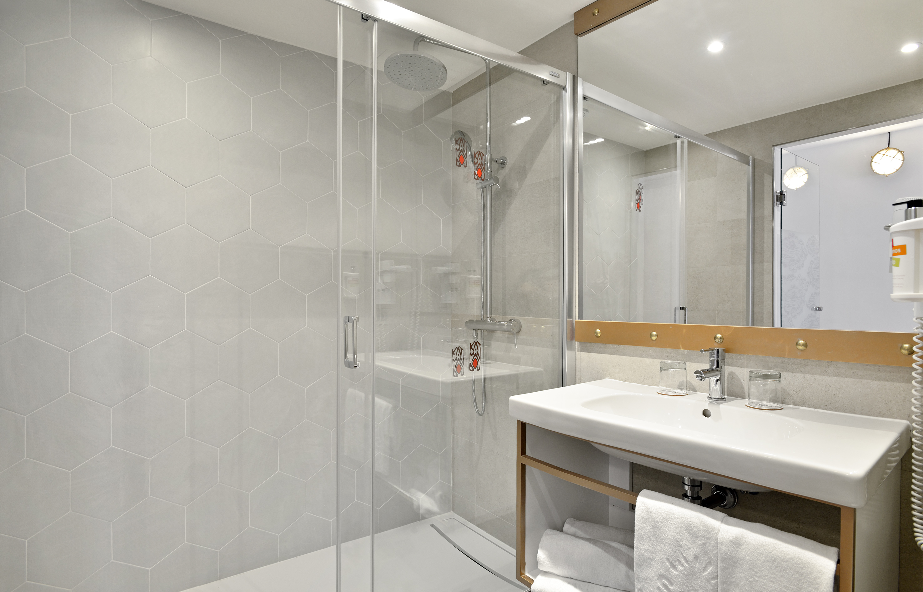Modern hotel bathroom with glass shower, hexagonal tiles, and vanity sink.