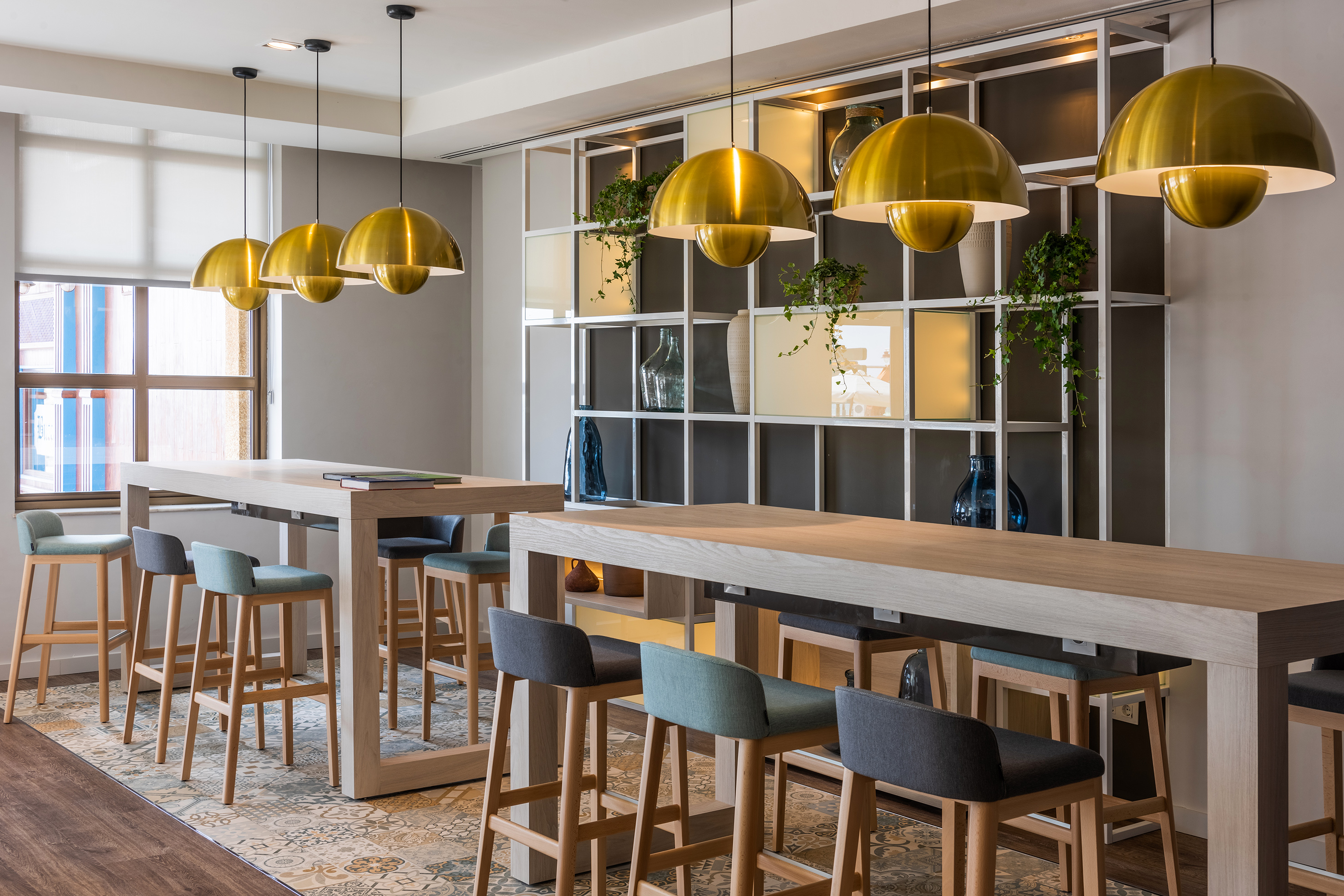 Modern cafe bar with high wooden tables, colorful stools, gold pendant lights.