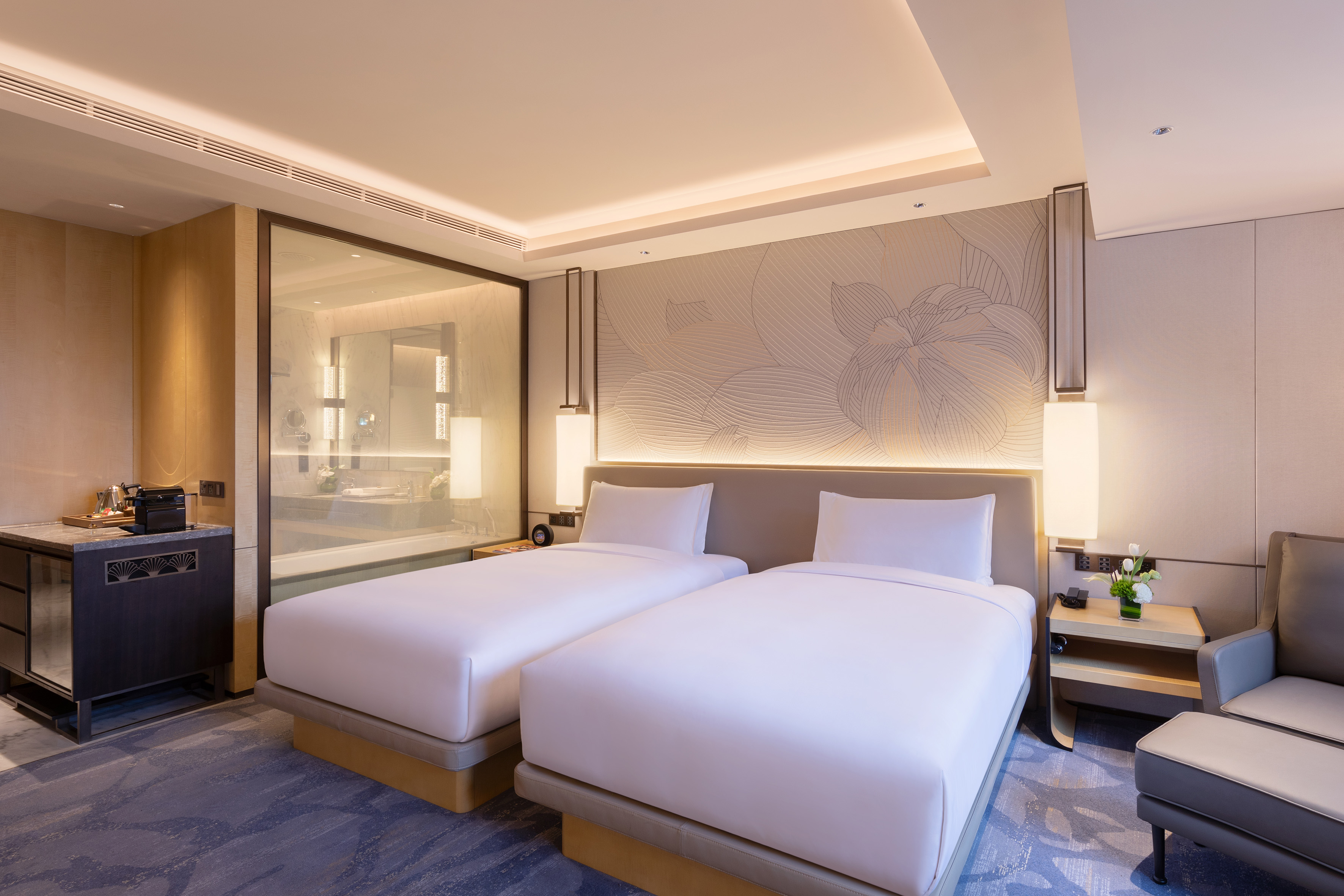 Elegant hotel twin room with modern design, floral headboard, and glass bathroom.
