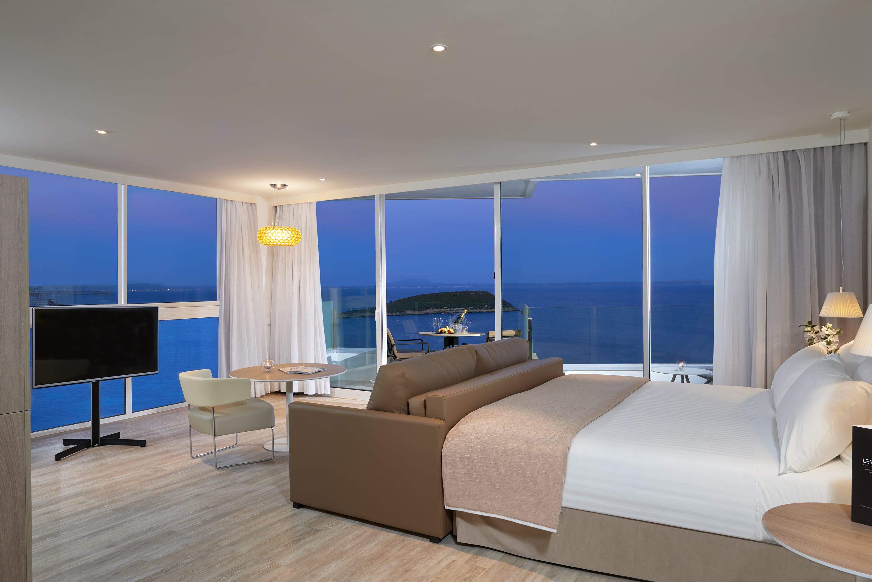 Luxury hotel suite with panoramic sea view, balcony, bed, and sofa.