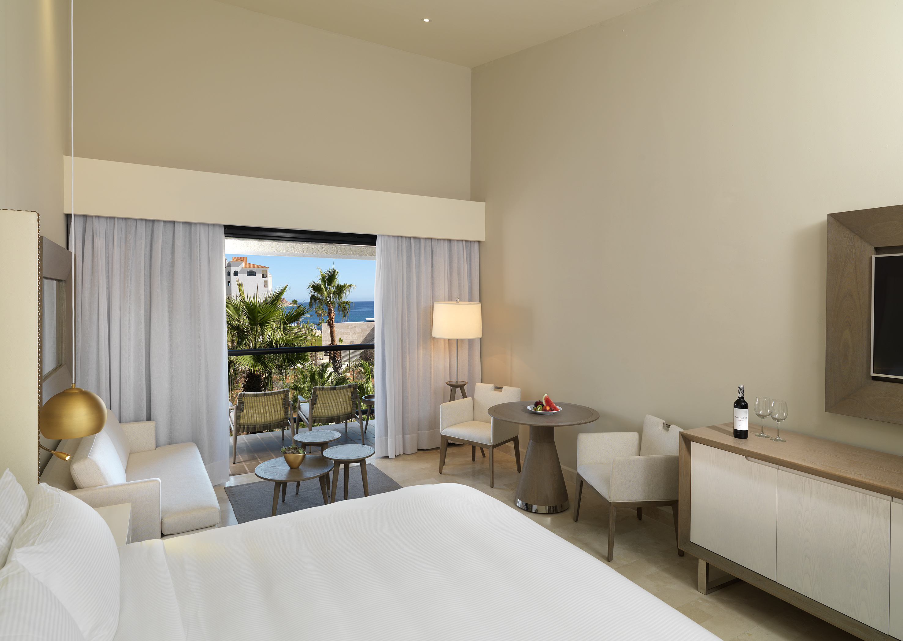 Modern resort room with king bed, ocean view balcony, and lounge area.