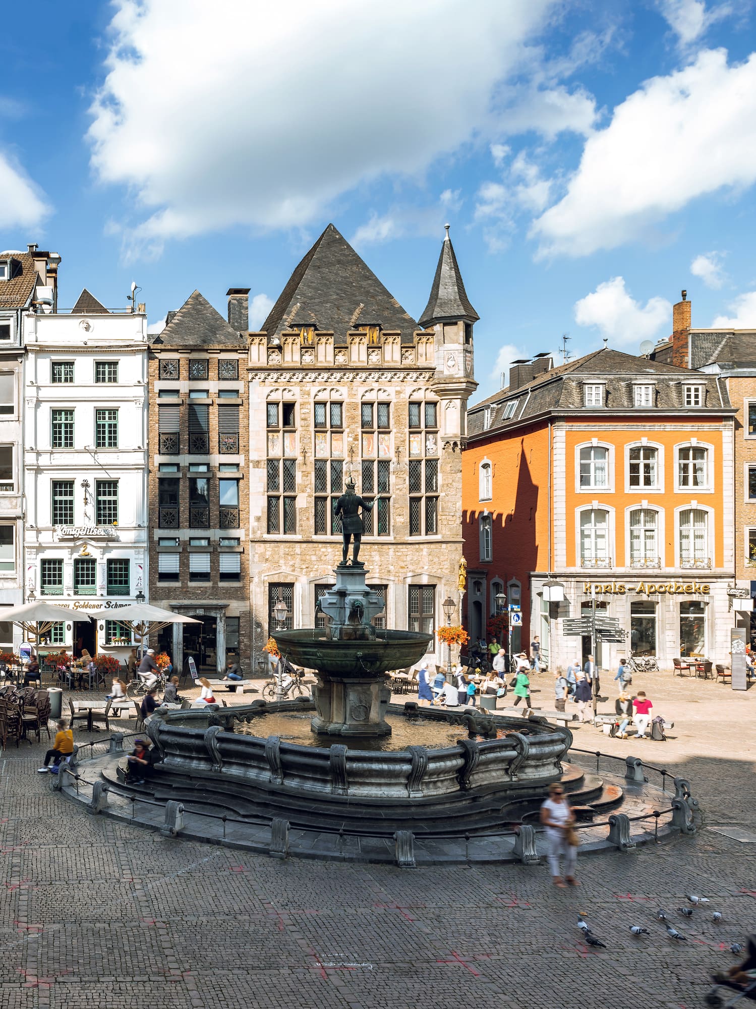 a fountain in a square with buildings and people walking around