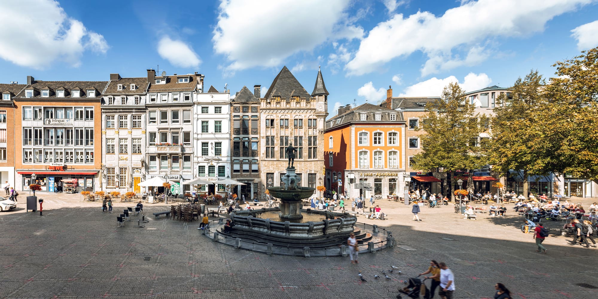 a fountain in a square with buildings and people walking around