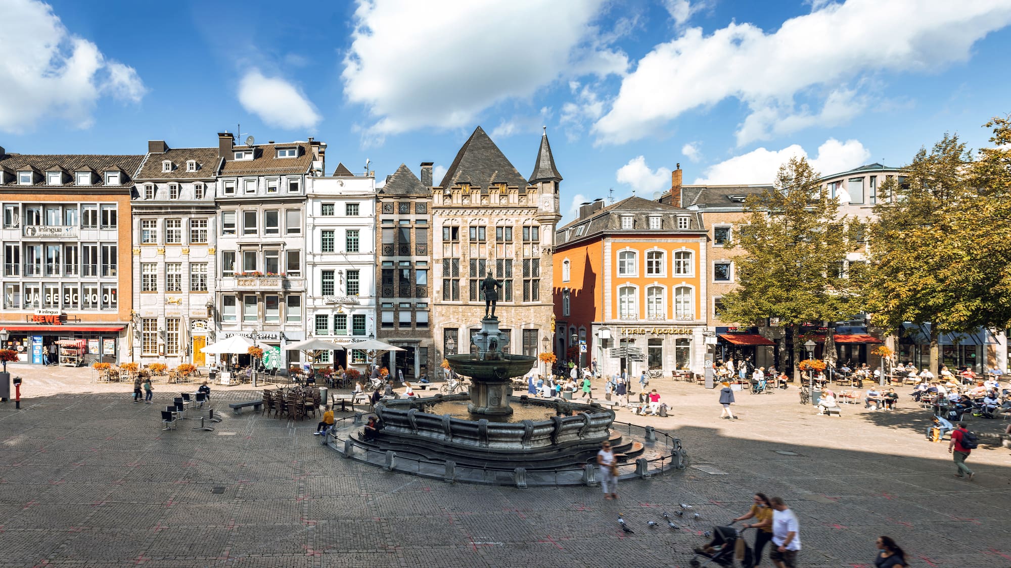 a fountain in a square with buildings and people walking around