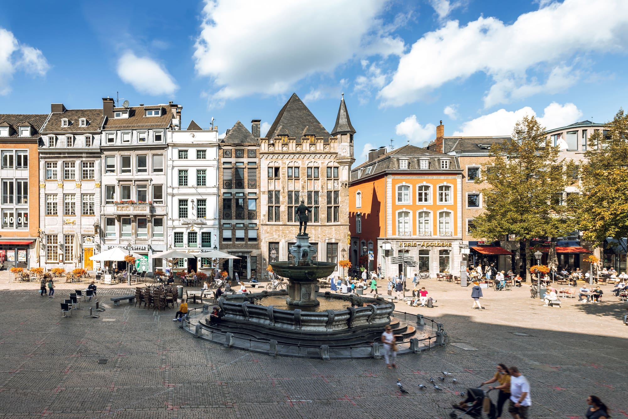 a fountain in a square with buildings and people walking around