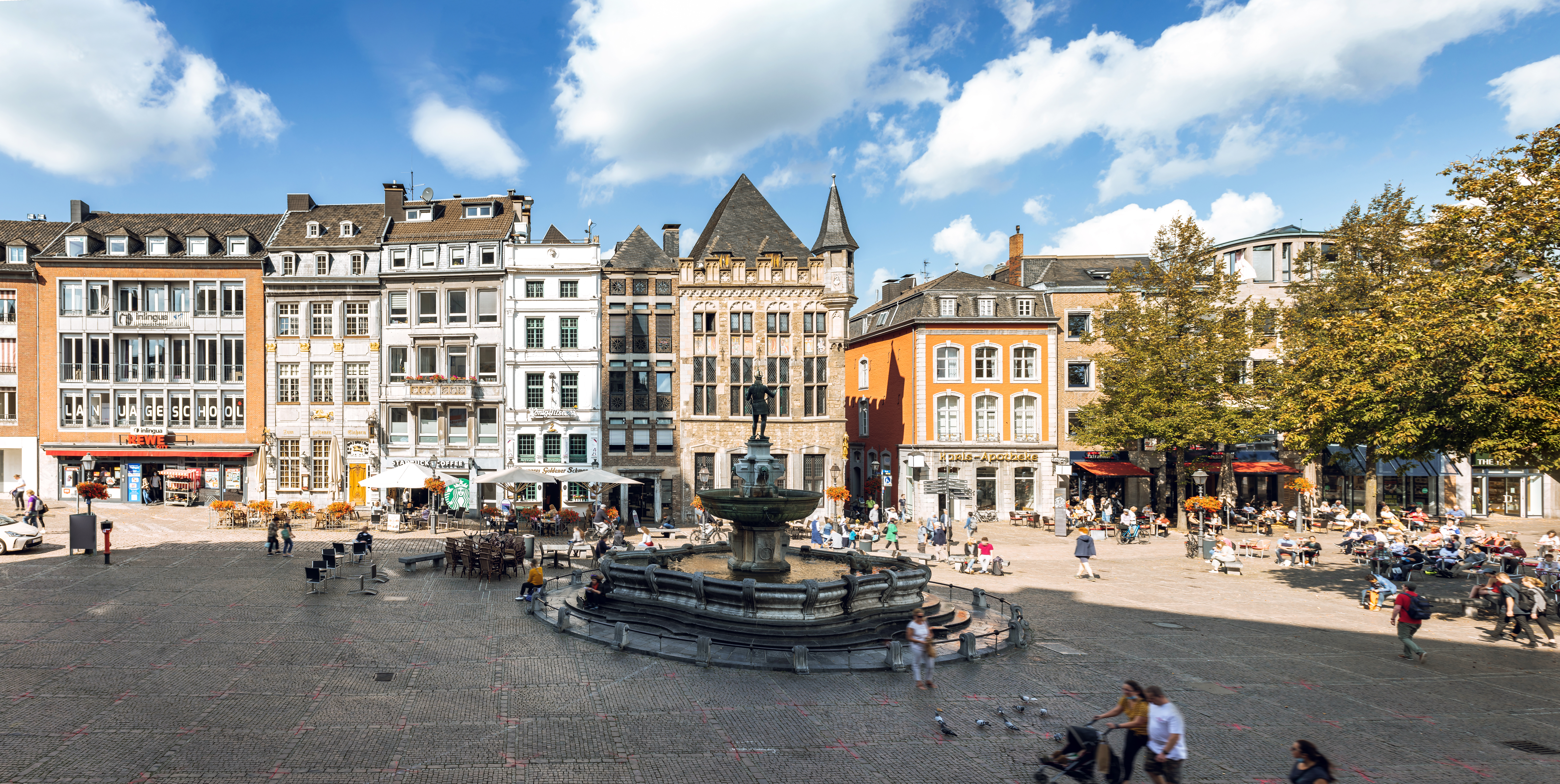 a fountain in a square with buildings and people walking around