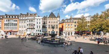 a fountain in a square with buildings and people walking around