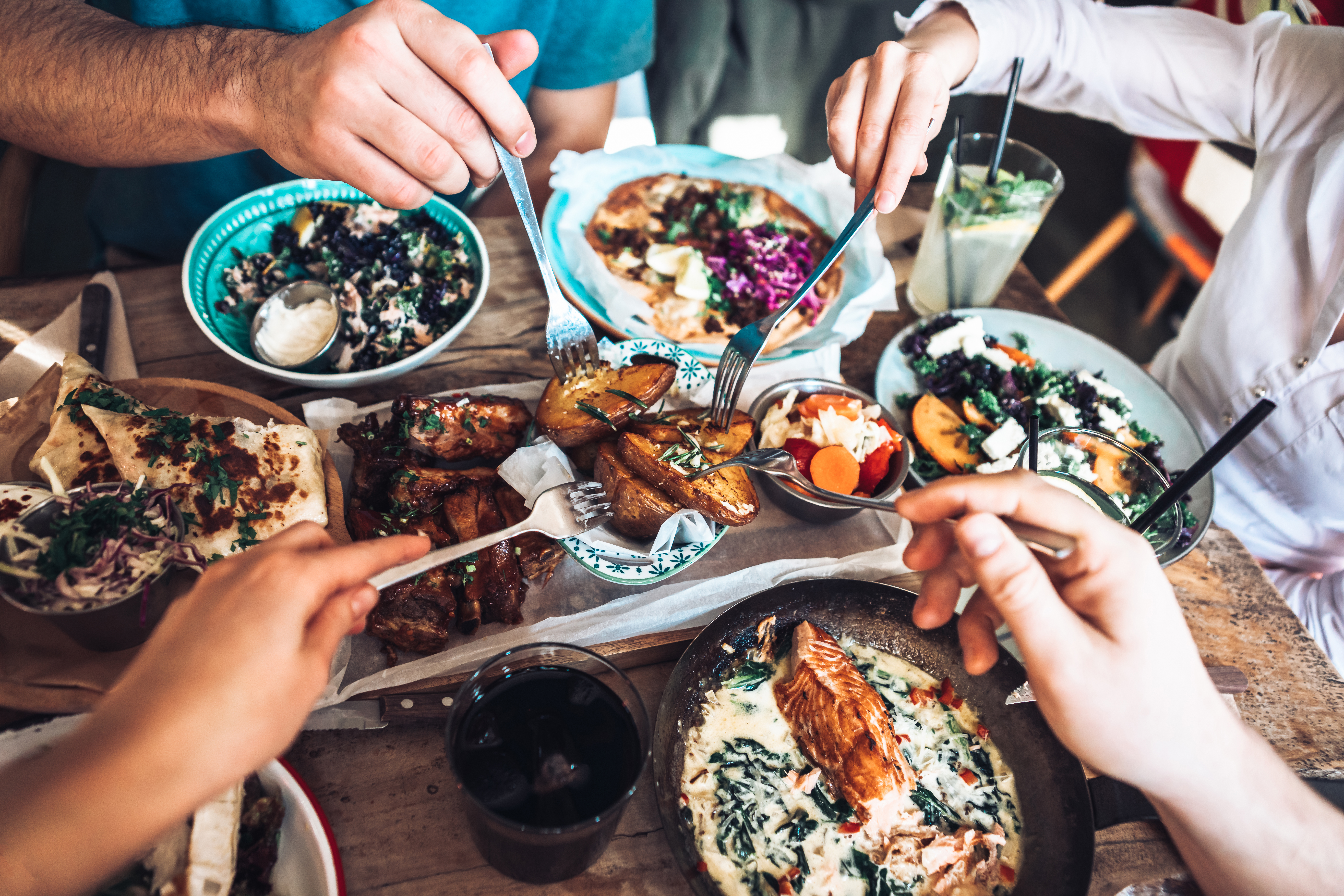 Friends sharing salmon, ribs, pizza, roasted potatoes, and fresh salads.