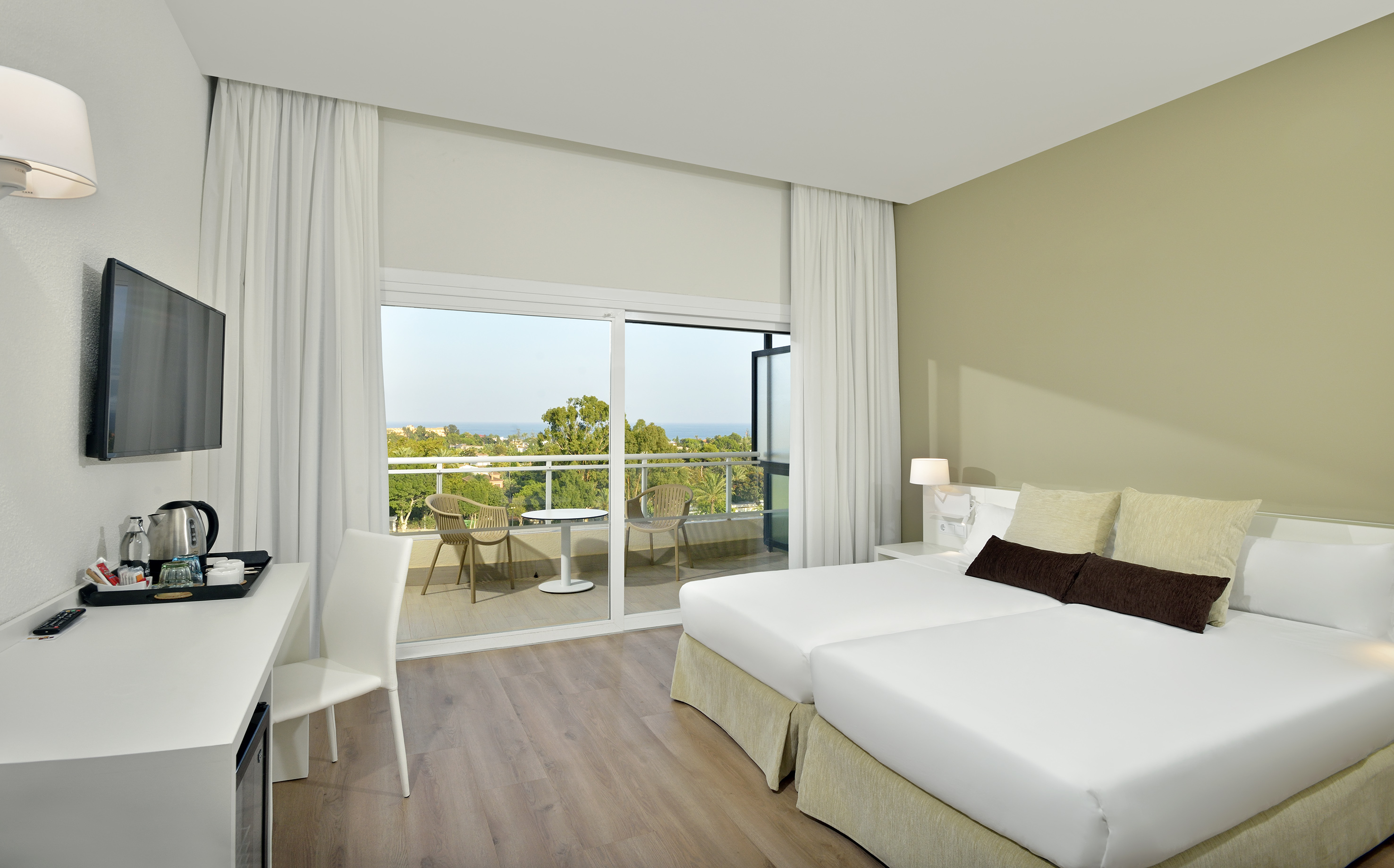 Modern hotel room with two twin beds, balcony, and ocean view.