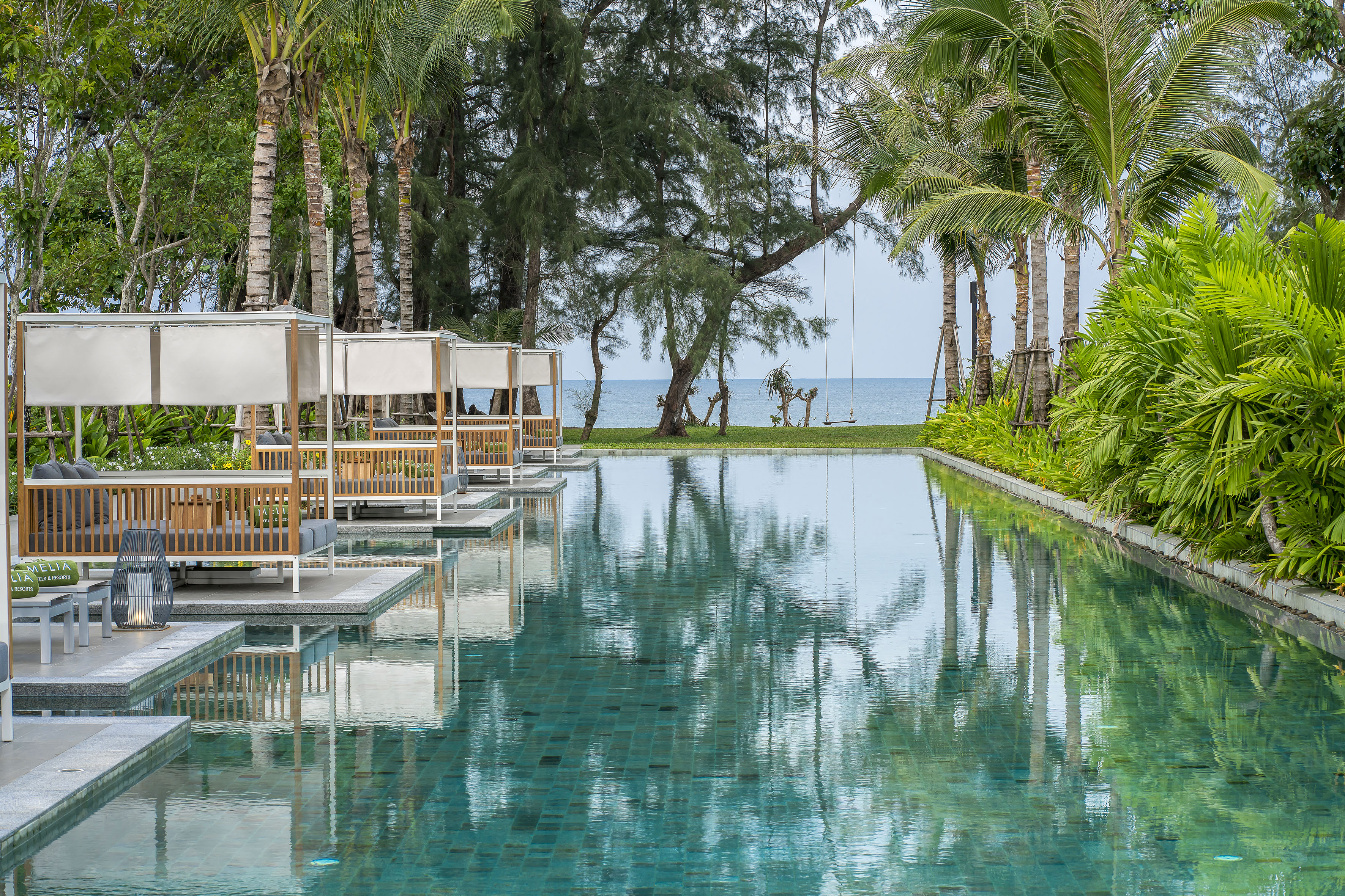 Tropical Melia resort pool with modern cabanas, palm trees, and ocean backdrop.