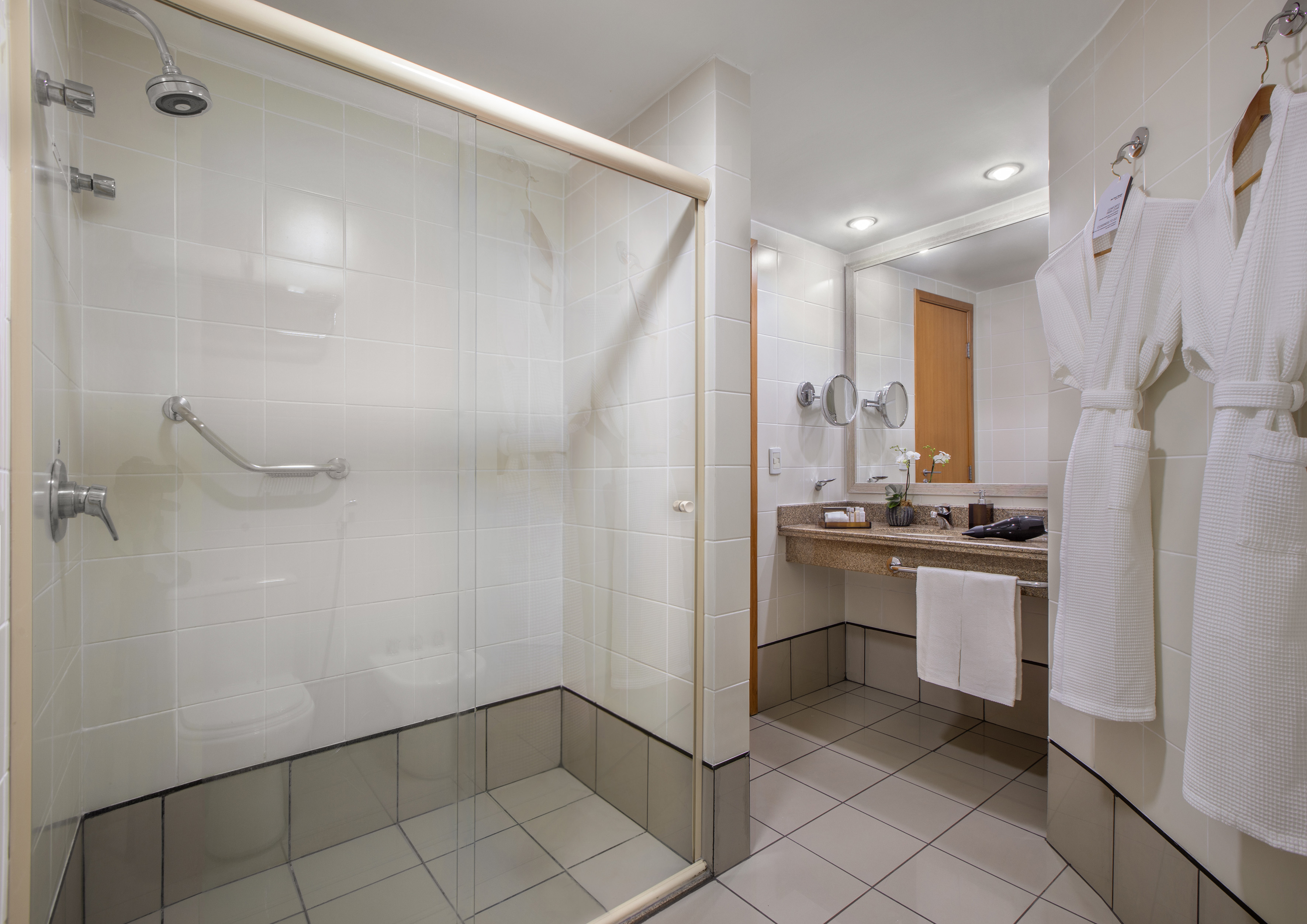 Accessible hotel bathroom with walk-in shower, vanity, and hanging bathrobes.