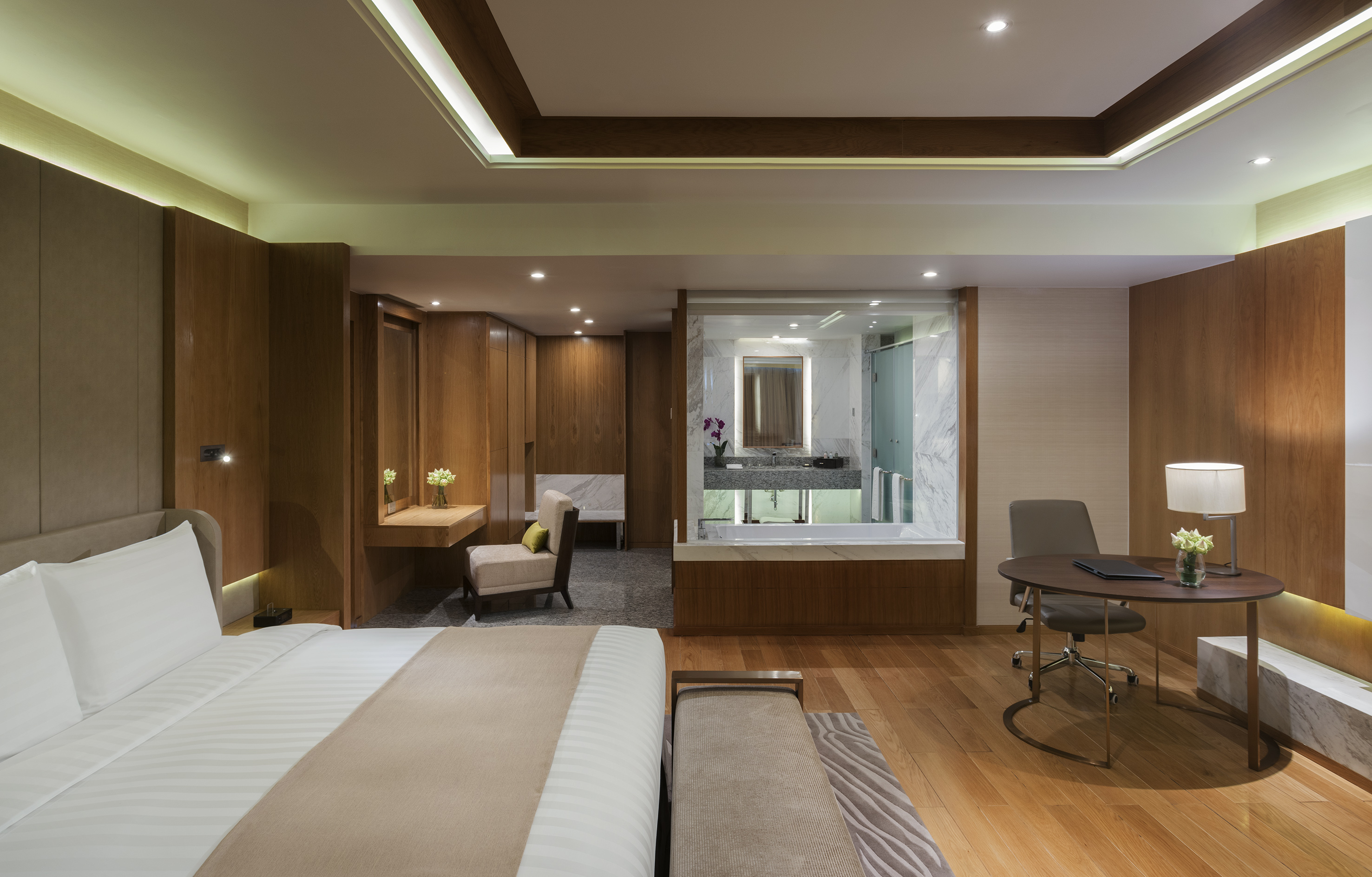 Modern luxury hotel room with king bed, open bathroom, and work desk.