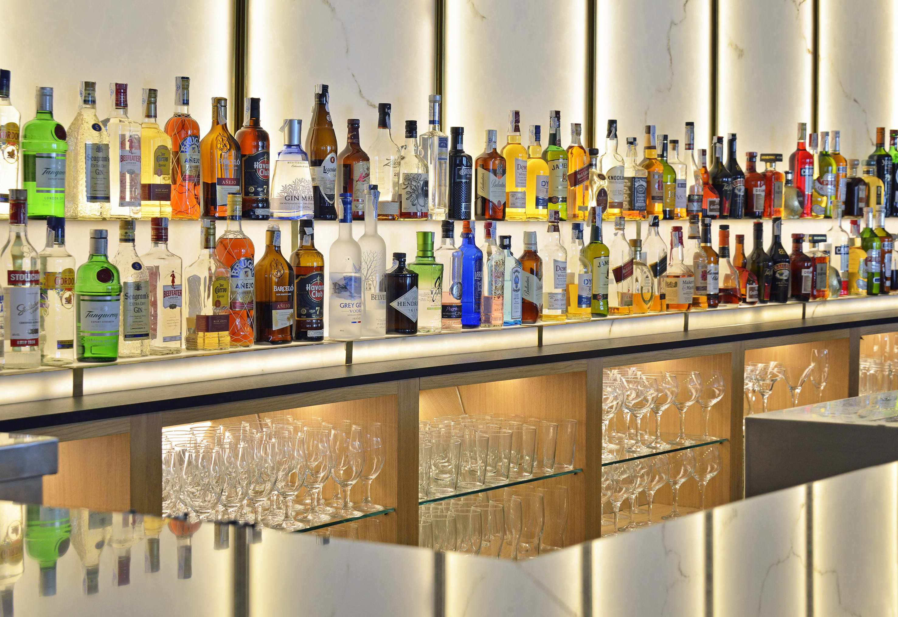 Illuminated bar with diverse liquor bottles, spirits, and sparkling glassware.