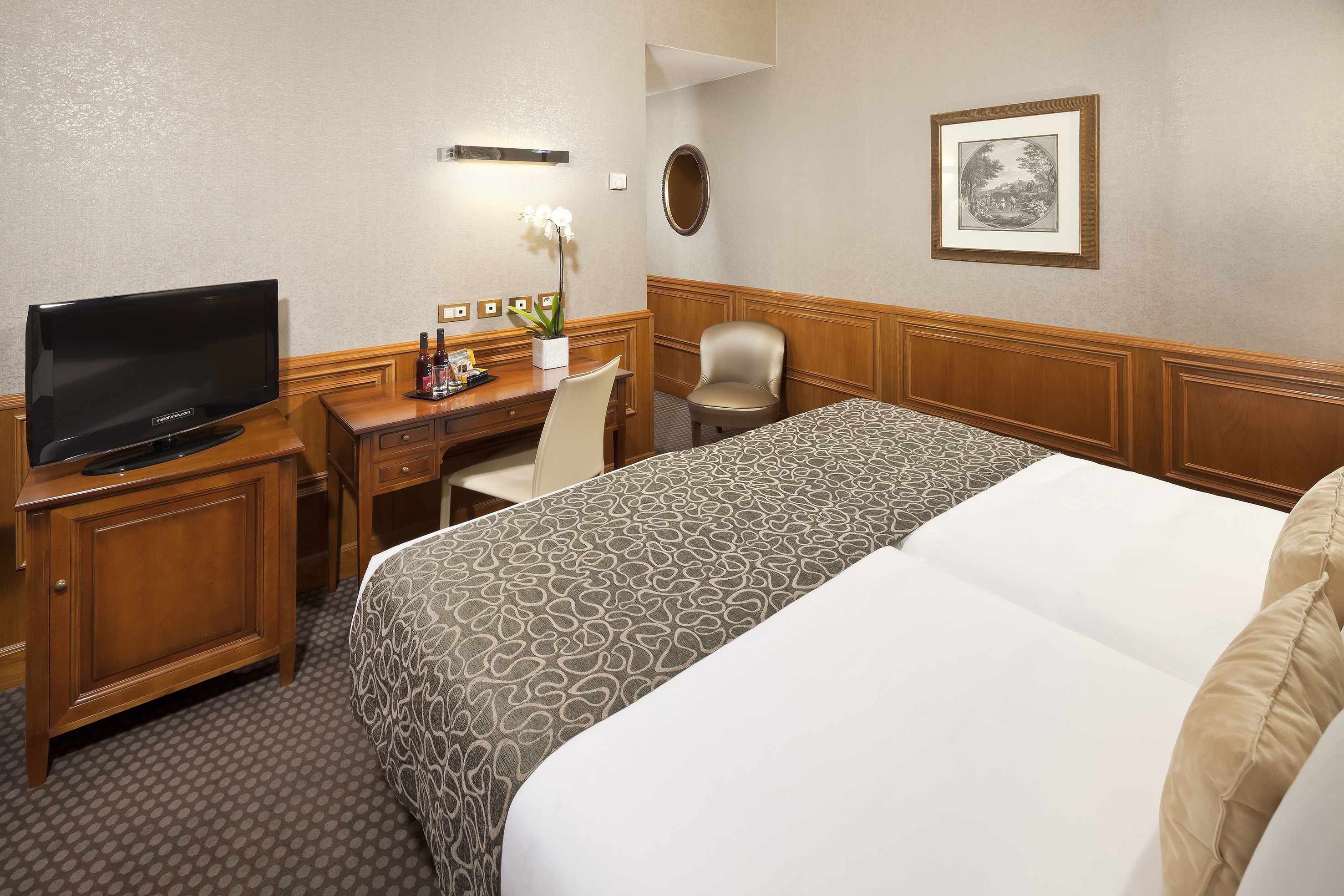 Hotel twin room with wooden desk, TV, and elegant wall paneling.