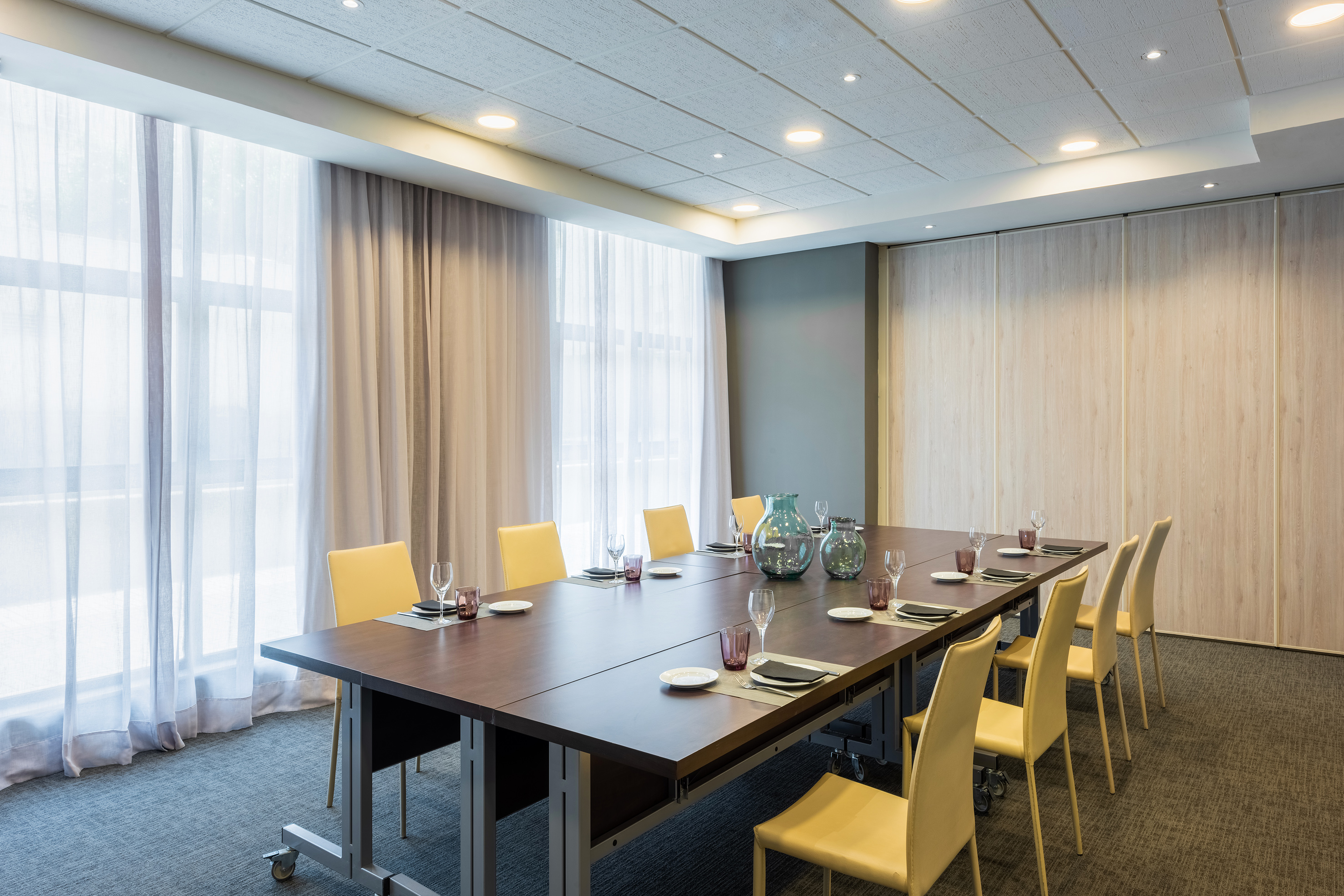 Modern conference room with long table, yellow chairs, and large windows.