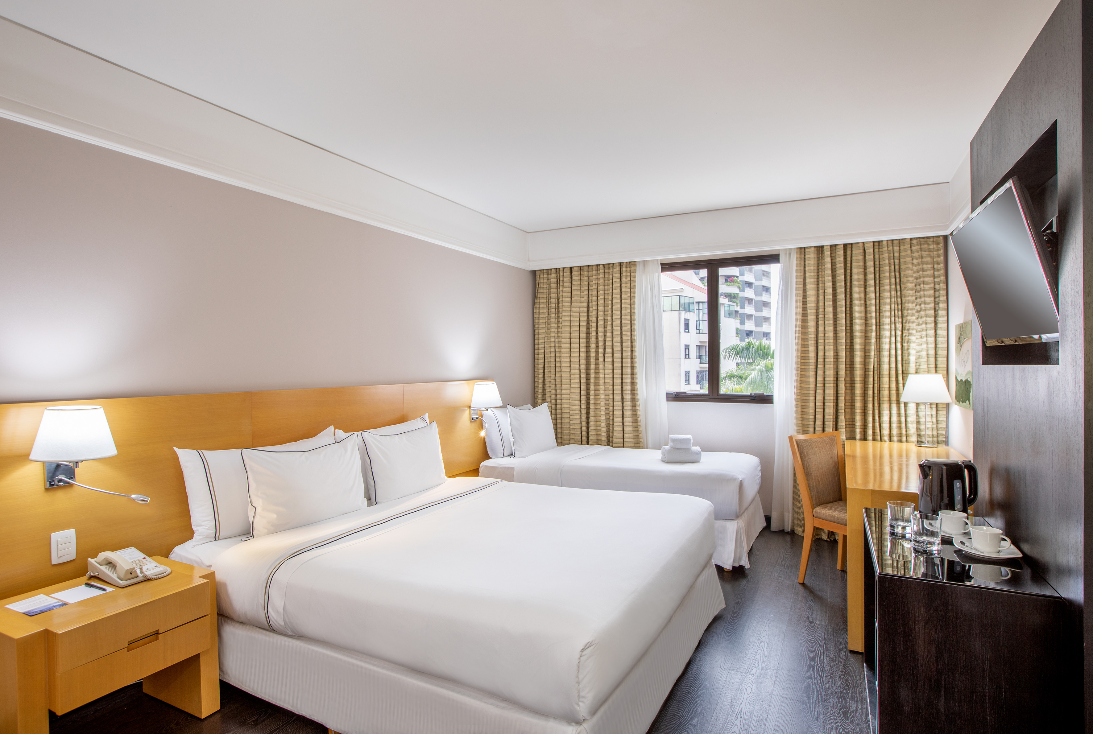 Modern hotel room with queen and twin beds, desk, TV, and window.