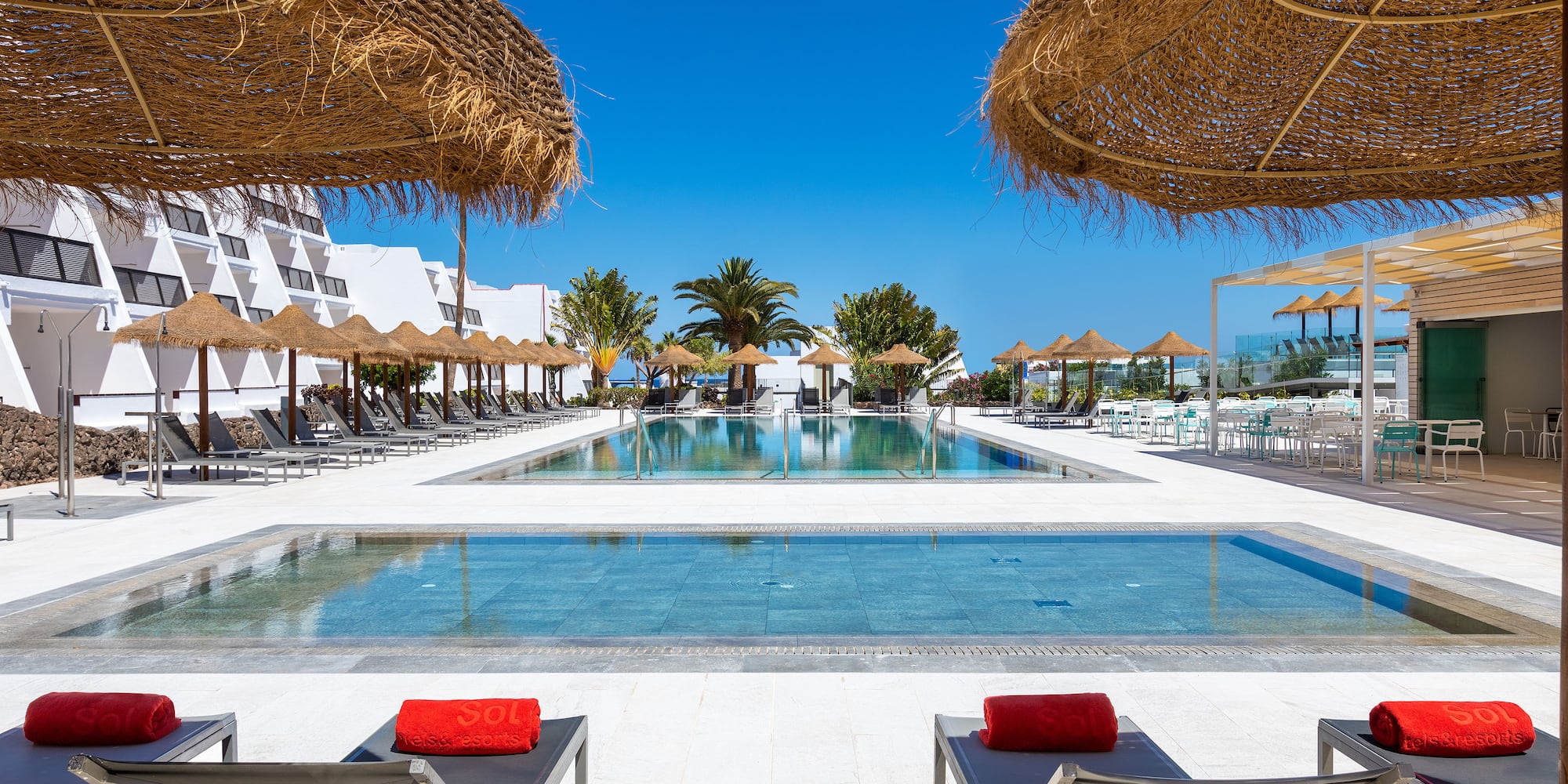 a pool with straw umbrellas and lounge chairs