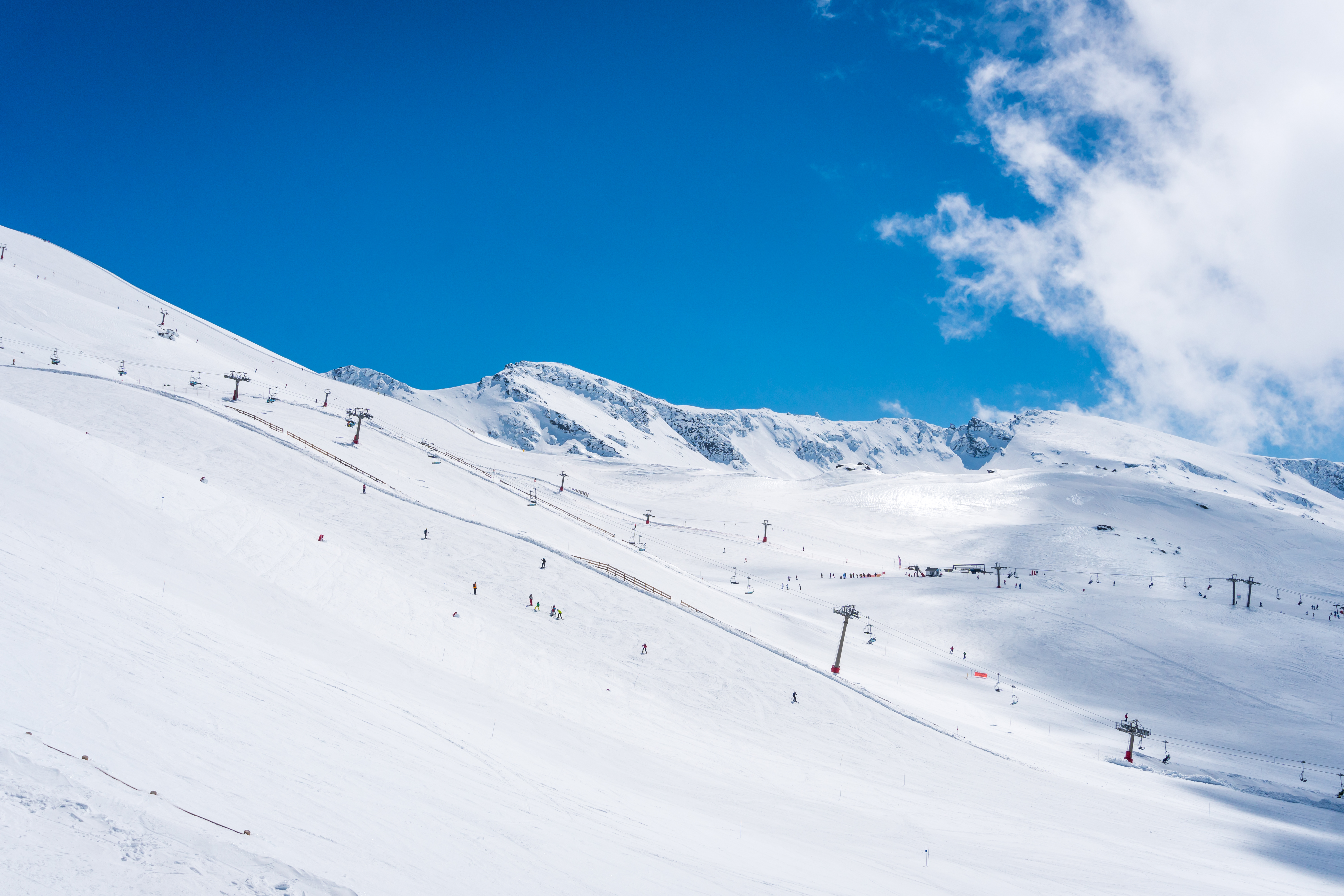 Skiers on a snow-covered mountain ski slope with ski lifts and distant peaks.