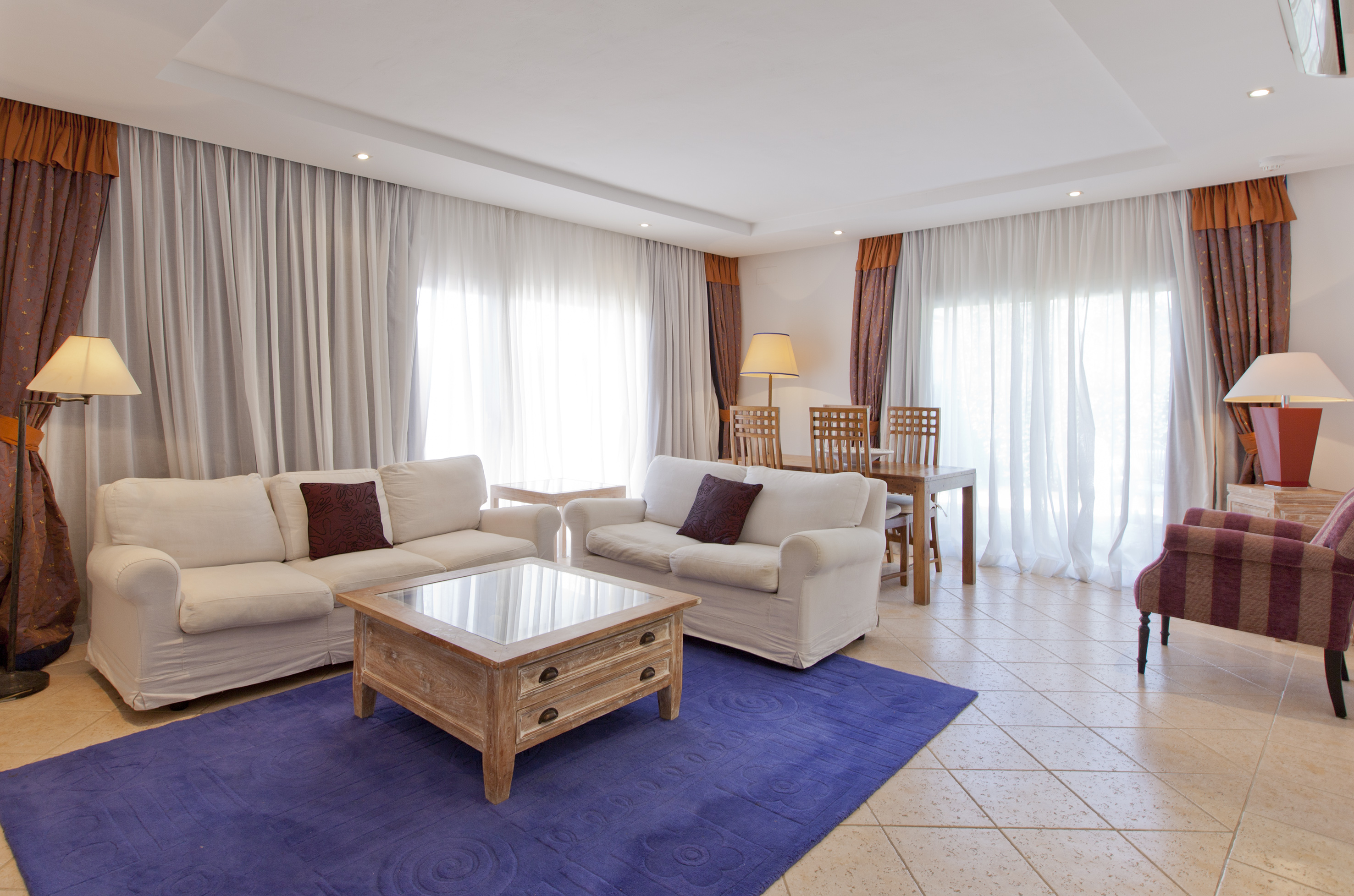 Living room with white sofas, purple rug, wooden coffee table, and dining table.