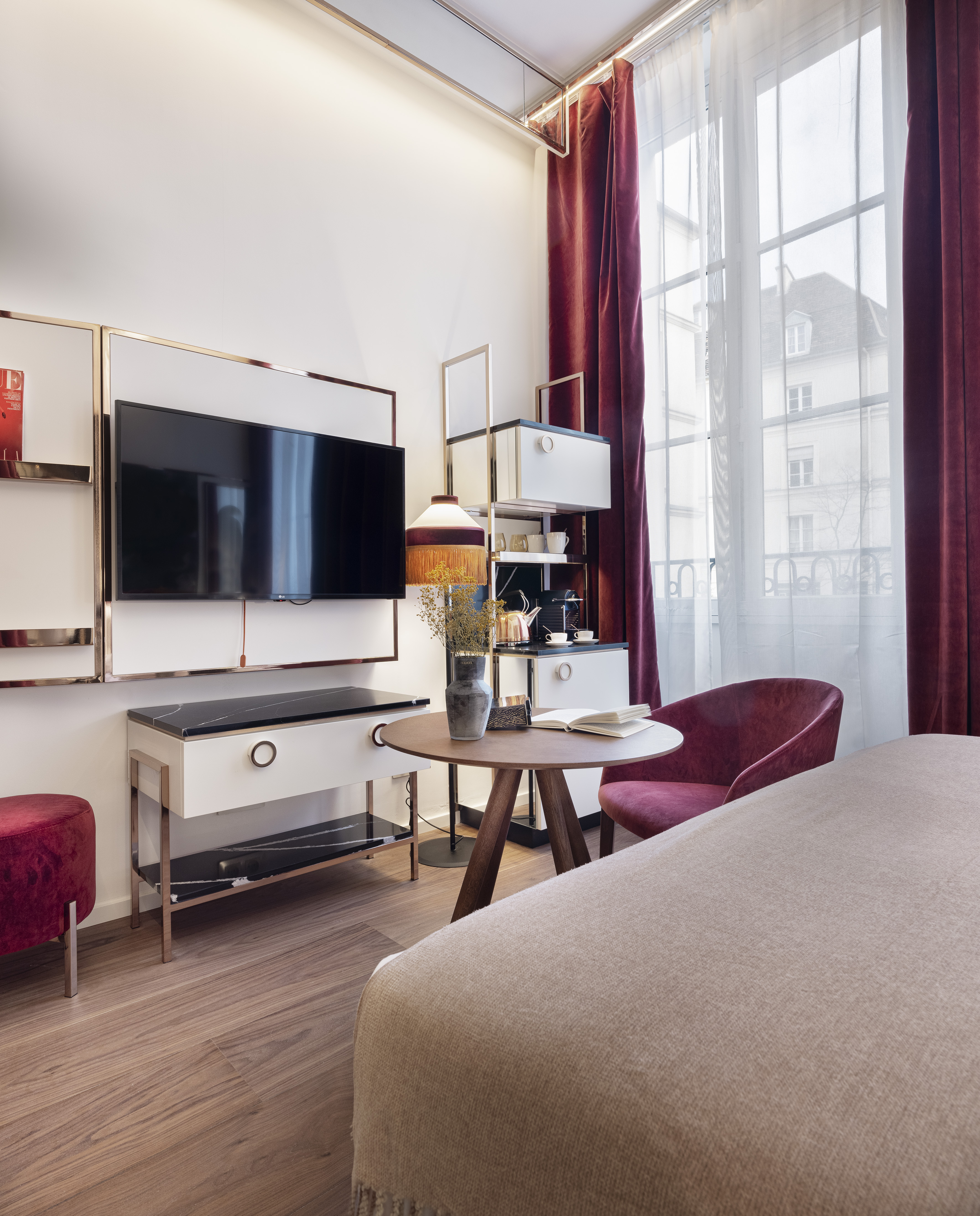 Modern hotel room: TV, bed, red armchair, gold accents, and large window.