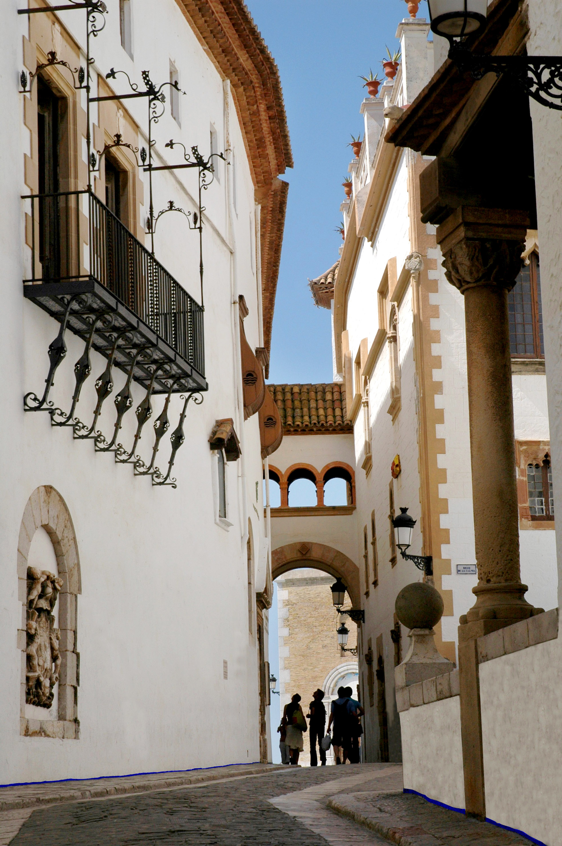 Historic European alley, white buildings, ornate iron balcony, stone archways.