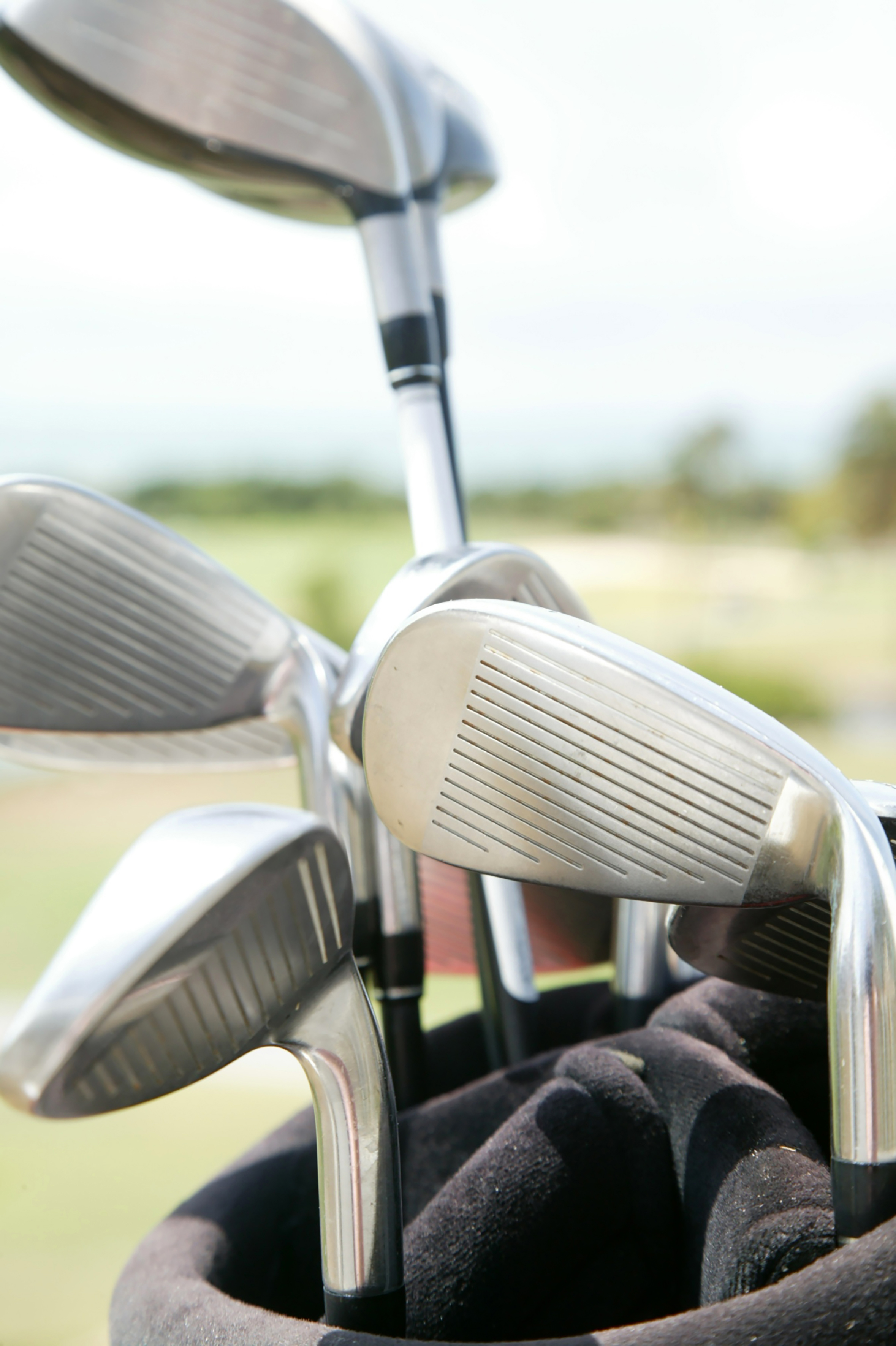 Shiny metal golf clubs, including irons, in a black bag on a green golf course.