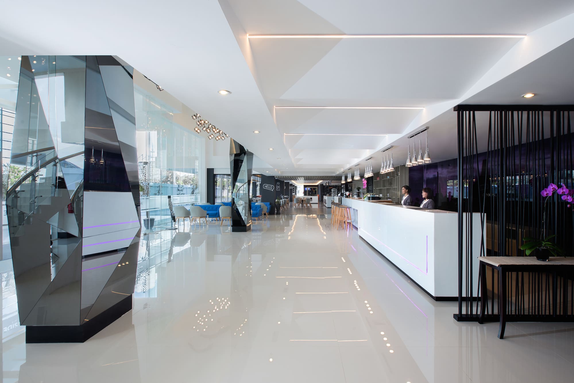 Modern hotel lobby with reception, staff, and glass staircase.