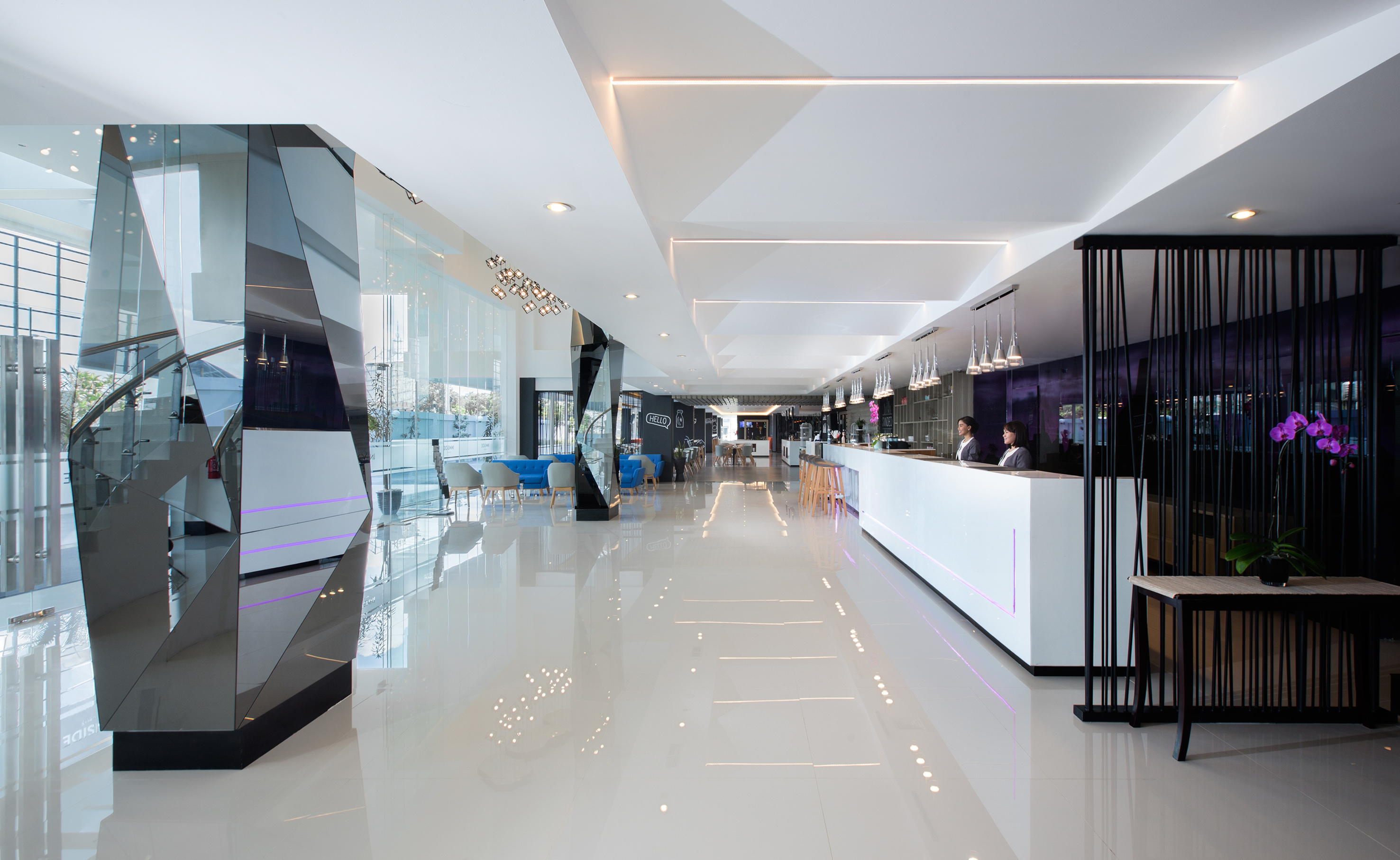 Modern hotel lobby with reception, staff, and glass staircase.