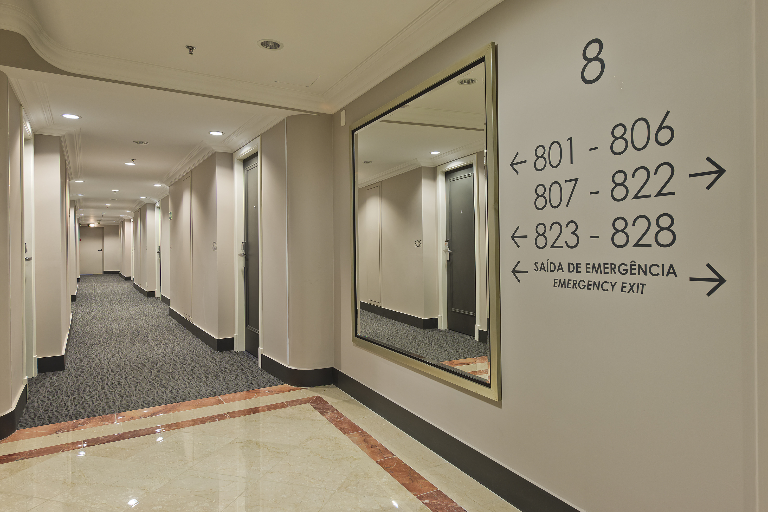 Bright hotel hallway with room number signs, mirror, and emergency exit. - Meliá Campinas, Campinas