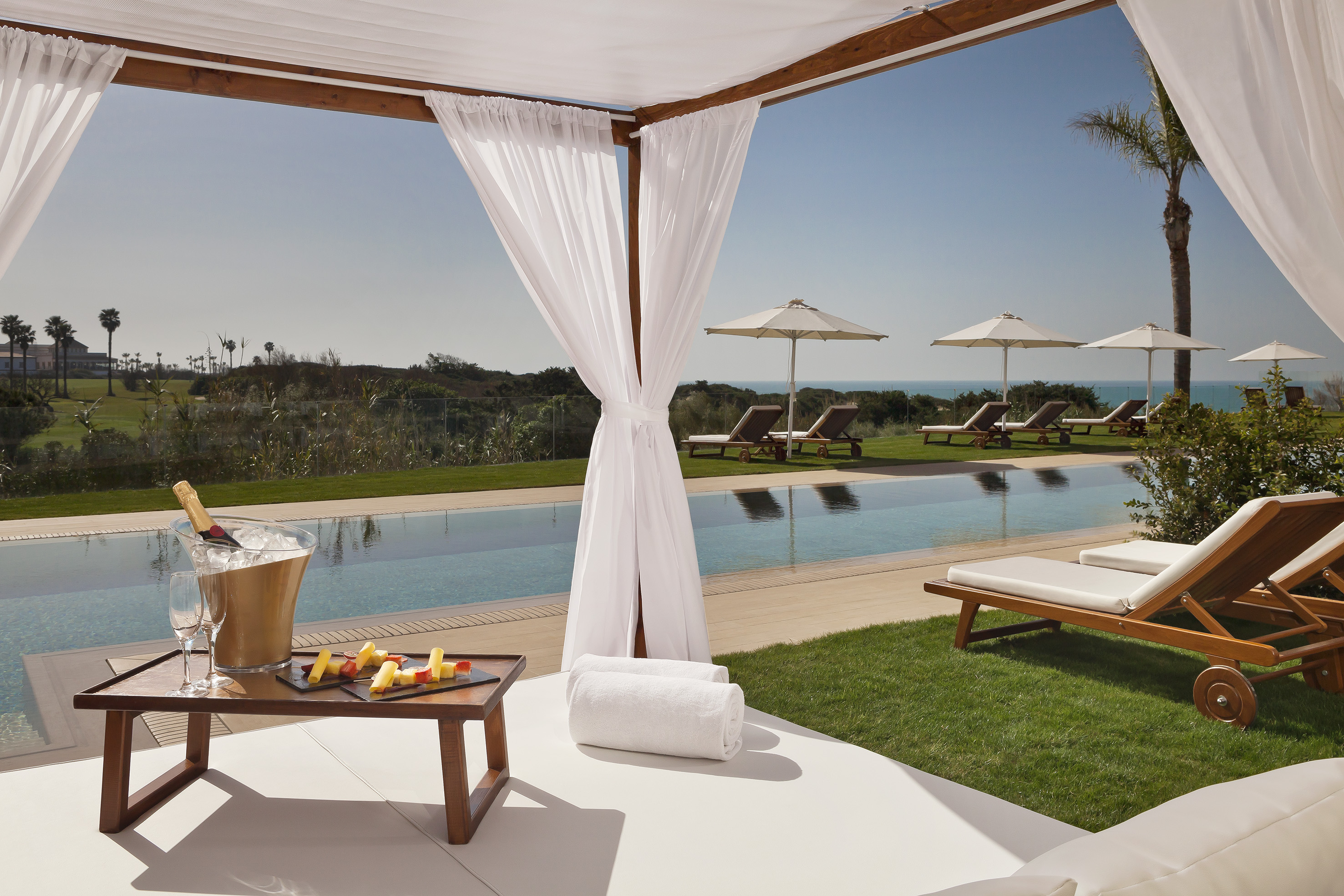 Luxury cabana by infinity pool with champagne, ocean view, and sun loungers.