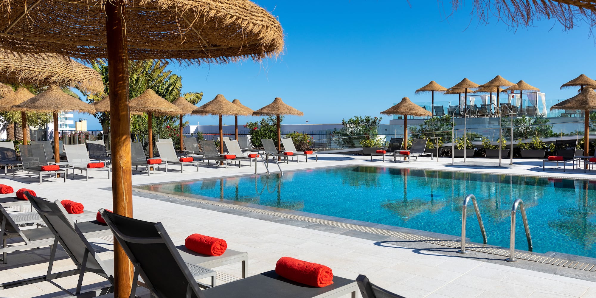 a pool with straw umbrellas and lounge chairs