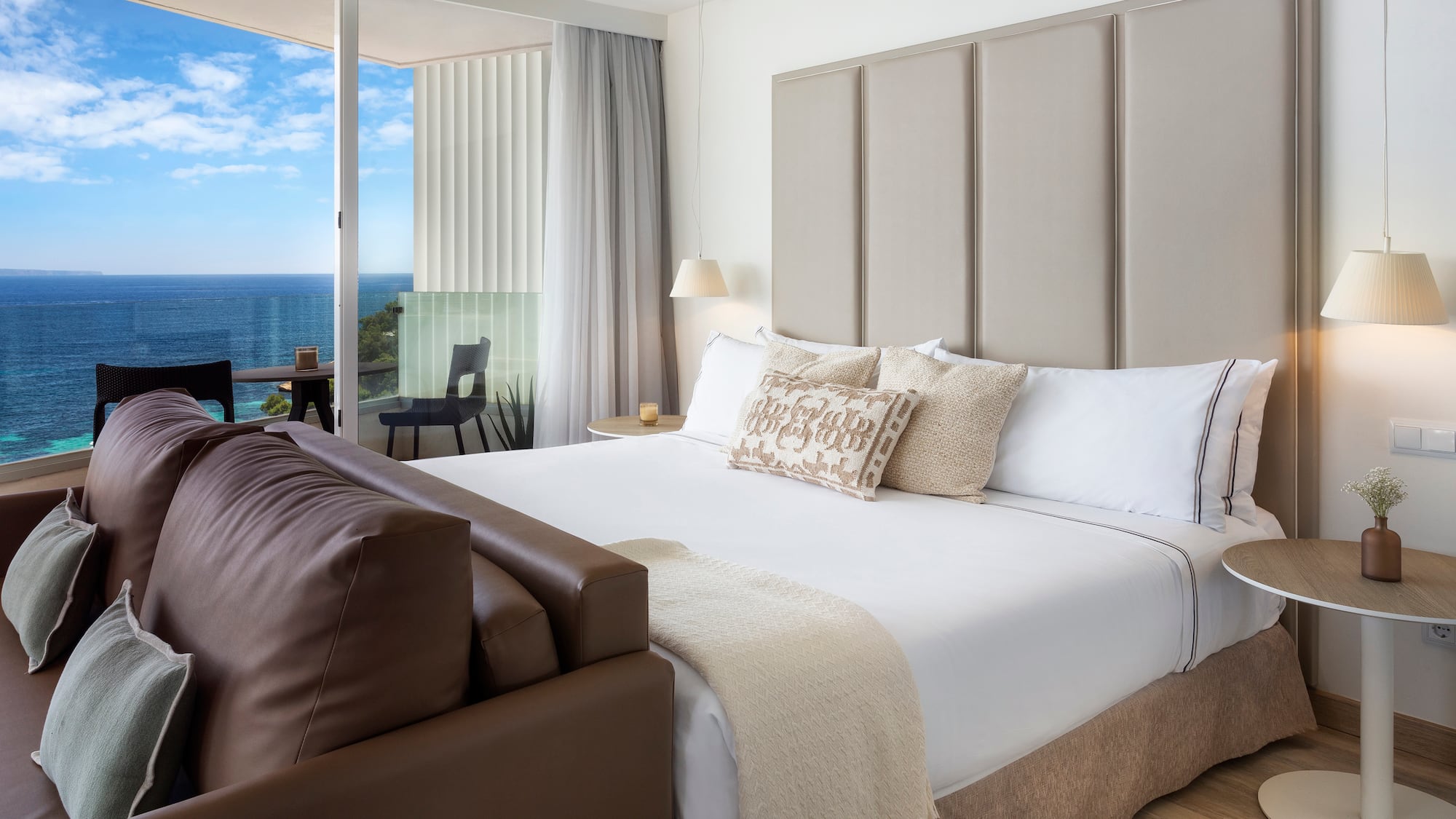 a bed with a leather couch and a chair in a room with a view of the ocean