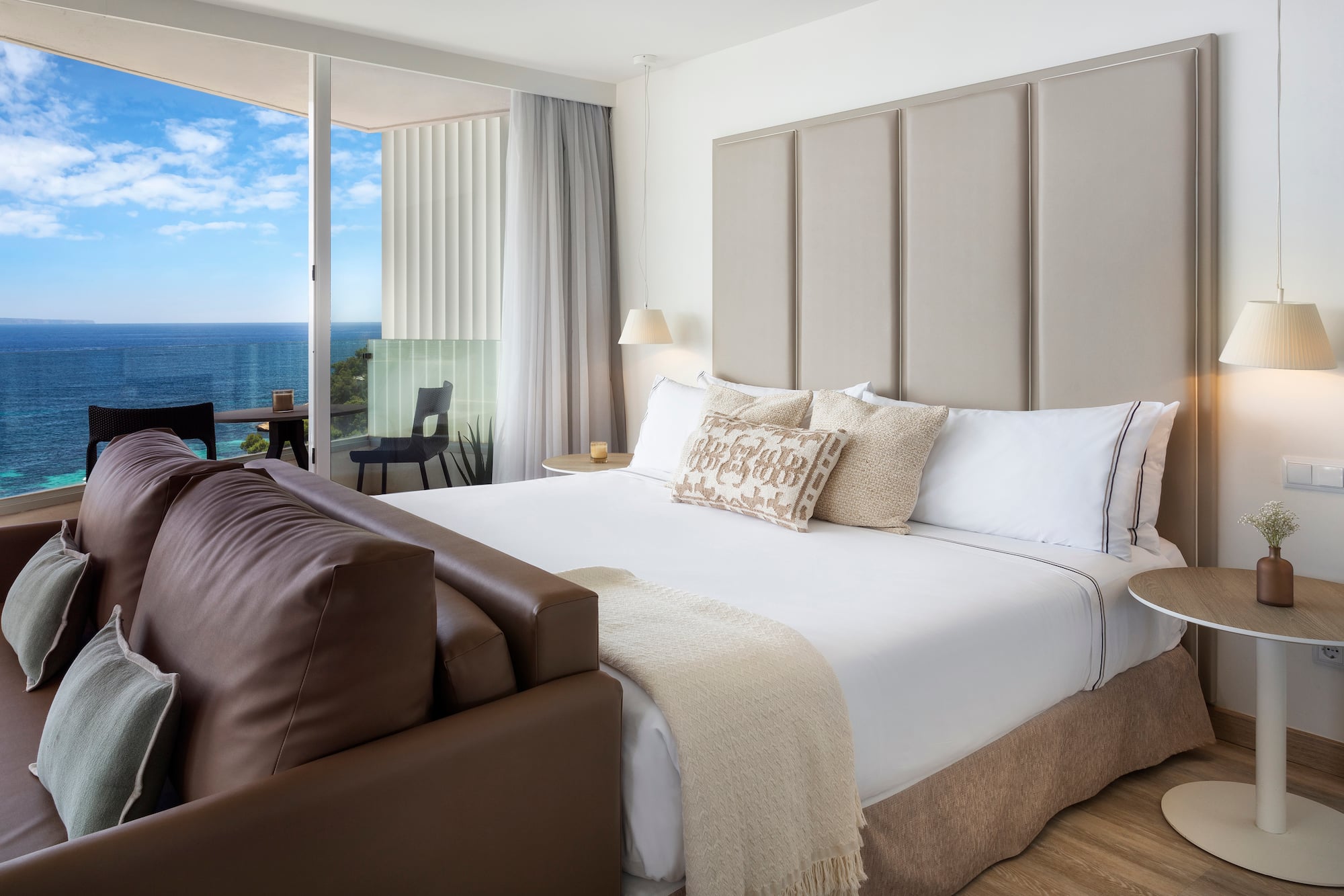 a bed with a leather couch and a chair in a room with a view of the ocean