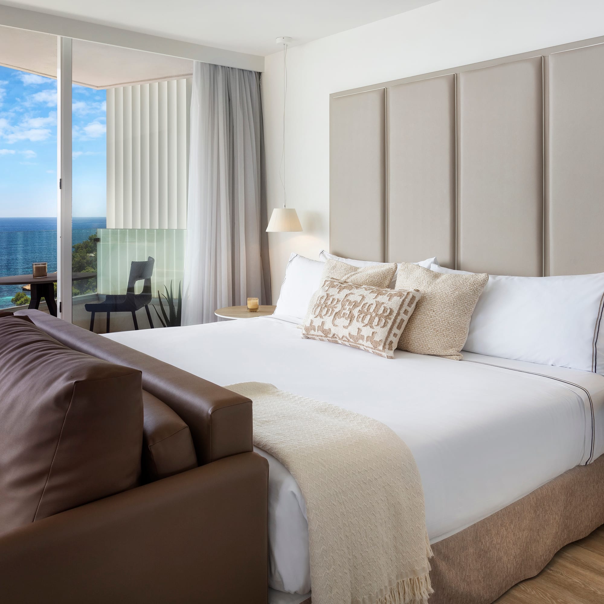 a bed with a leather couch and a chair in a room with a view of the ocean