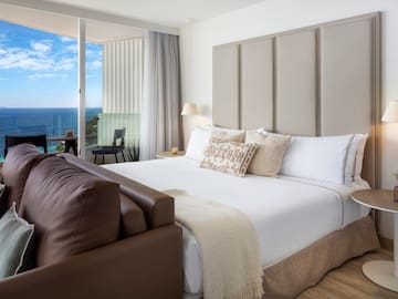 a bed with a leather couch and a chair in a room with a view of the ocean
