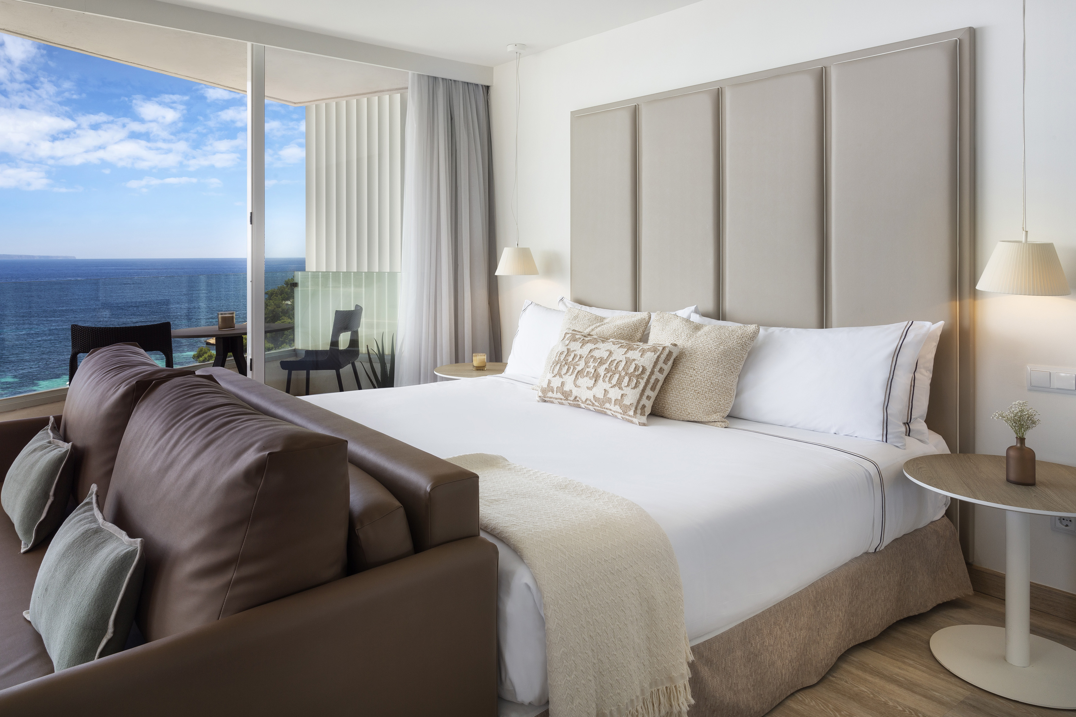 a bed with a leather couch and a chair in a room with a view of the ocean