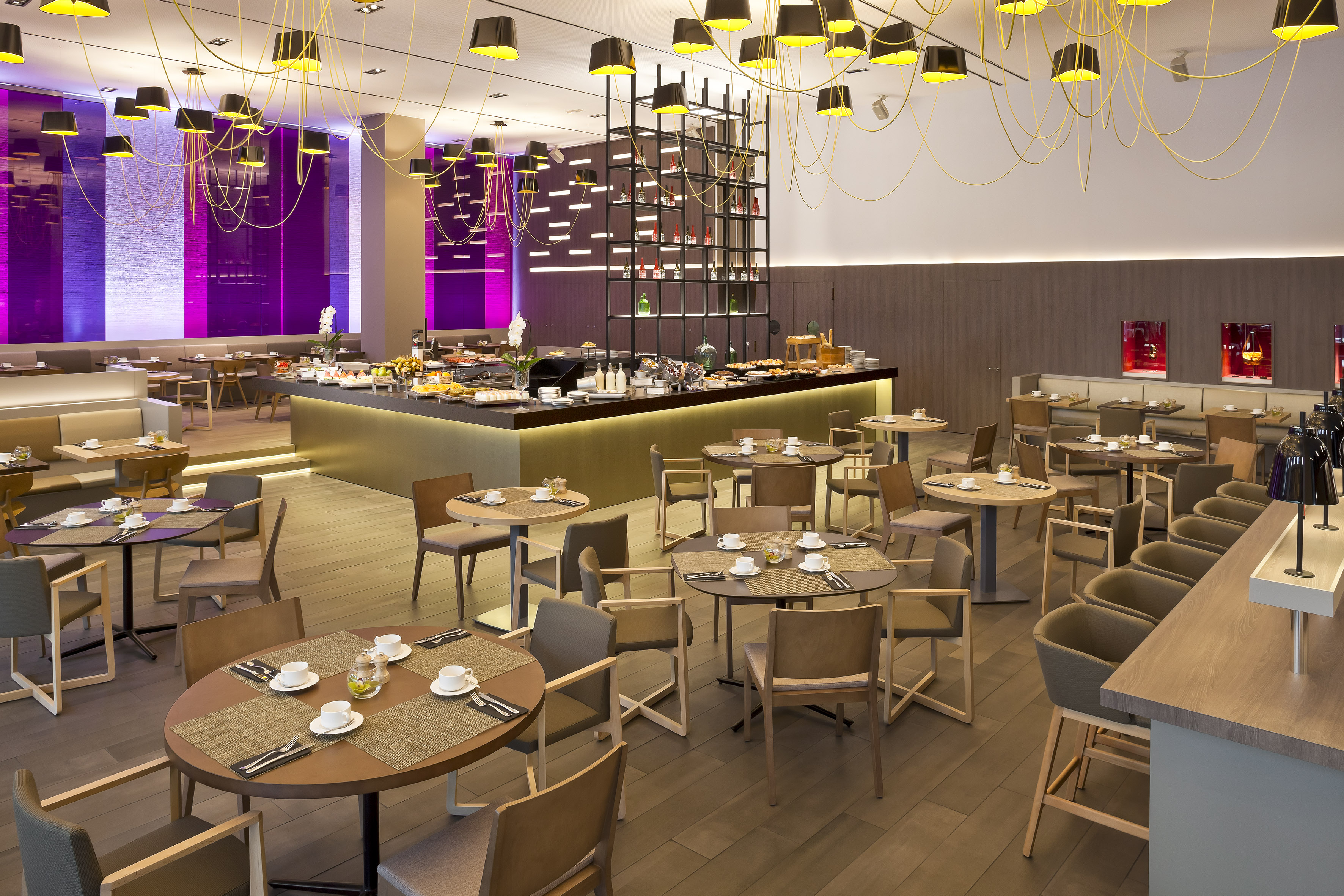 Modern hotel dining room with breakfast buffet and contemporary seating.