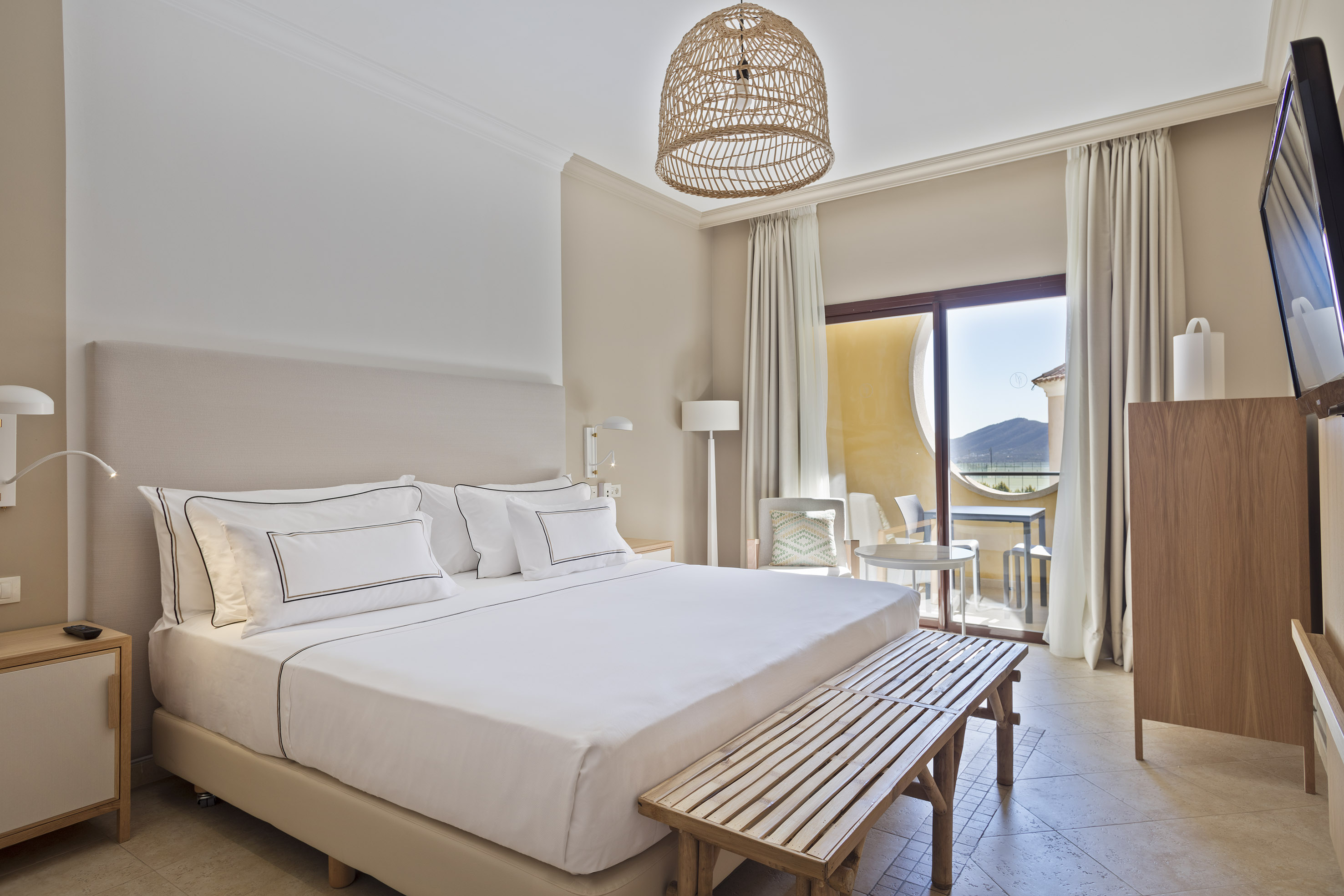 Modern hotel bedroom with king bed, woven light, and balcony mountain view.