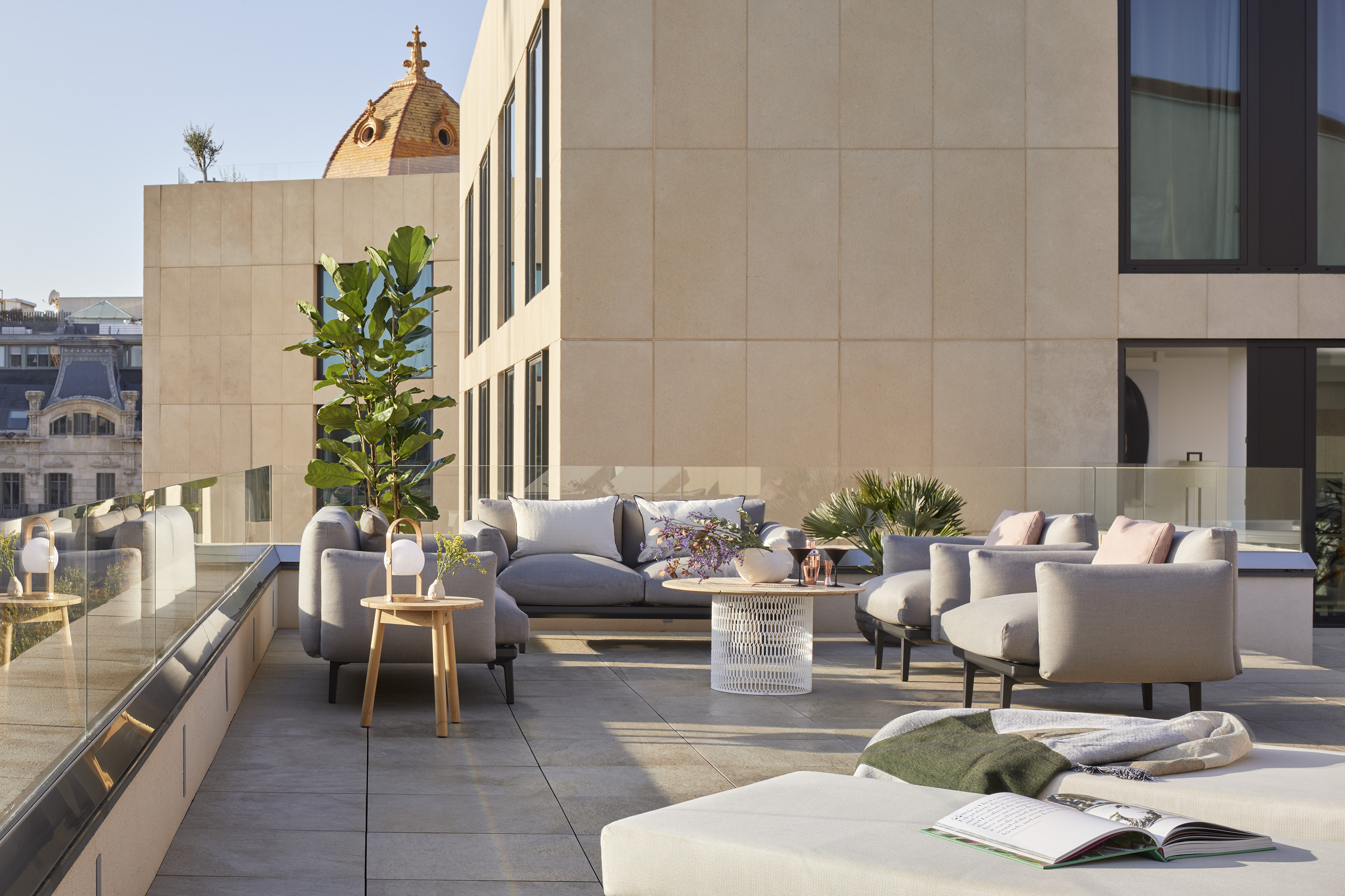 Modern outdoor lounge on a rooftop terrace with grey furniture and city views.