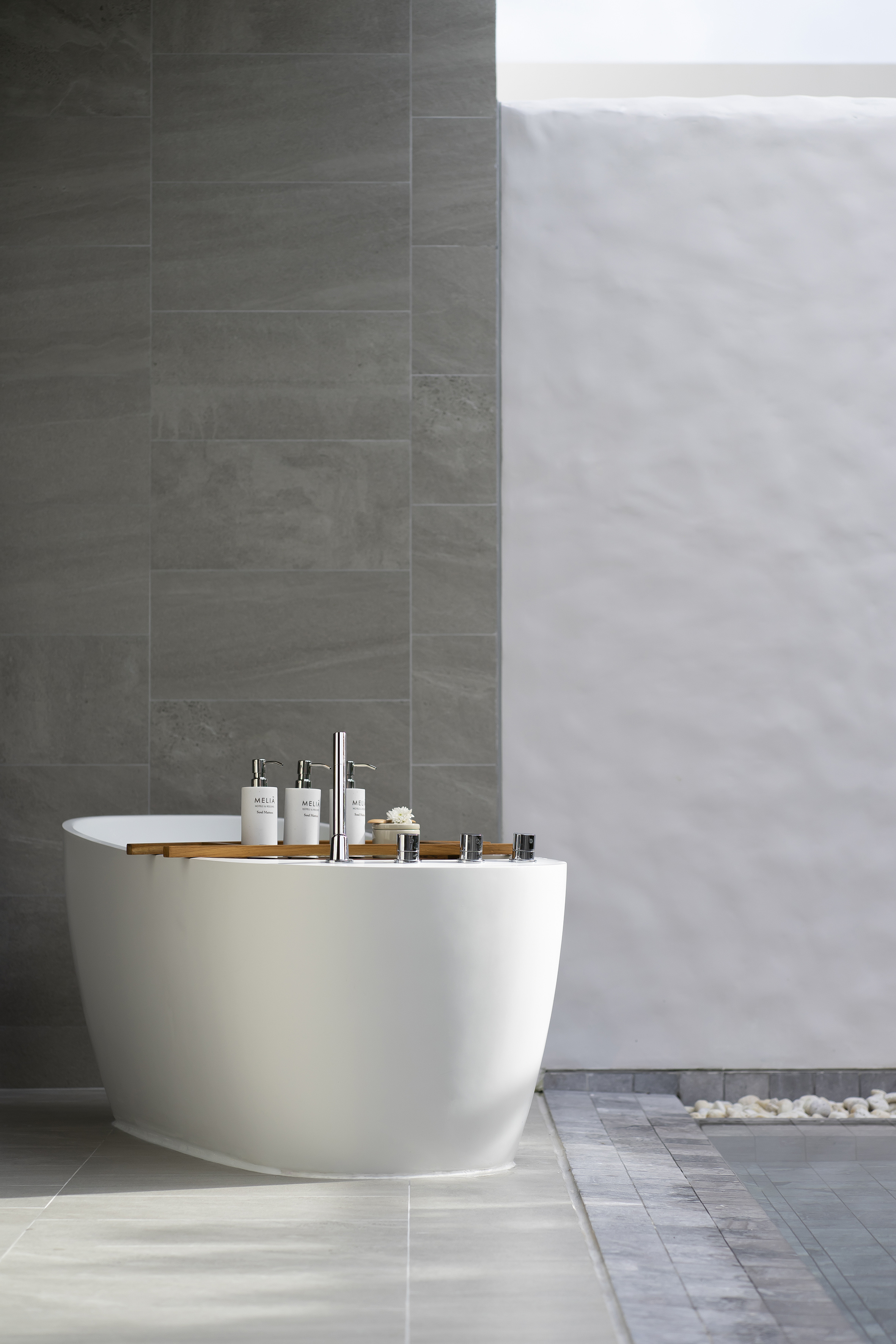 Freestanding bathtub with wooden caddy, toiletries, modern grey bathroom.