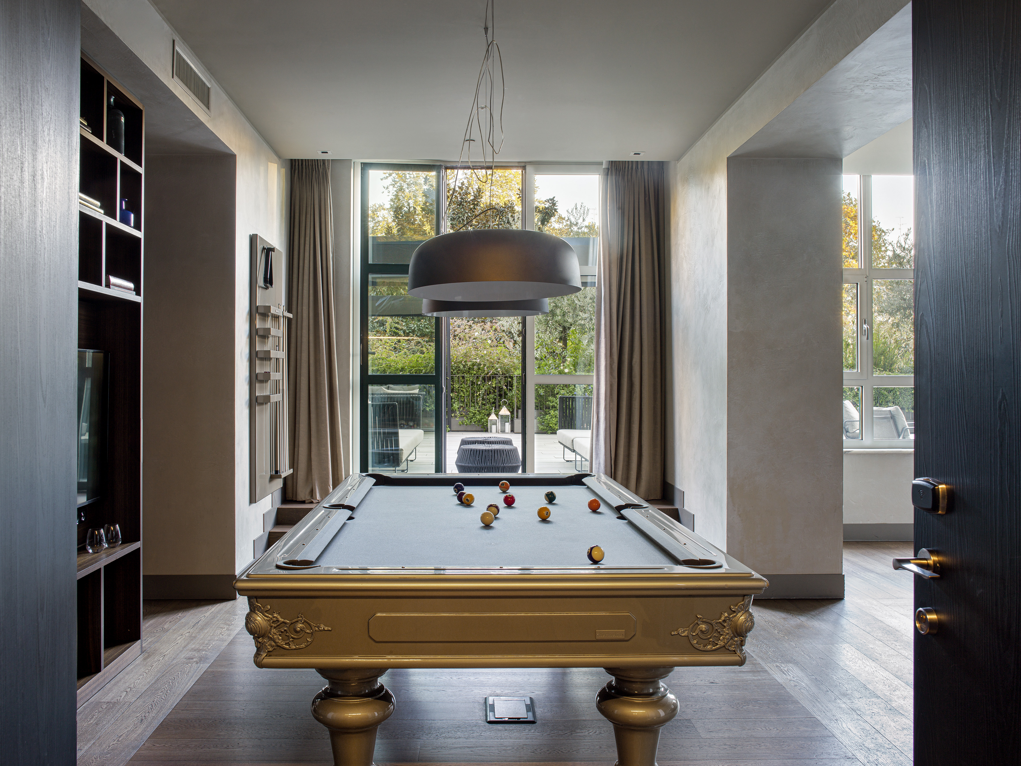 Modern luxury game room with an ornate golden pool table and large windows.