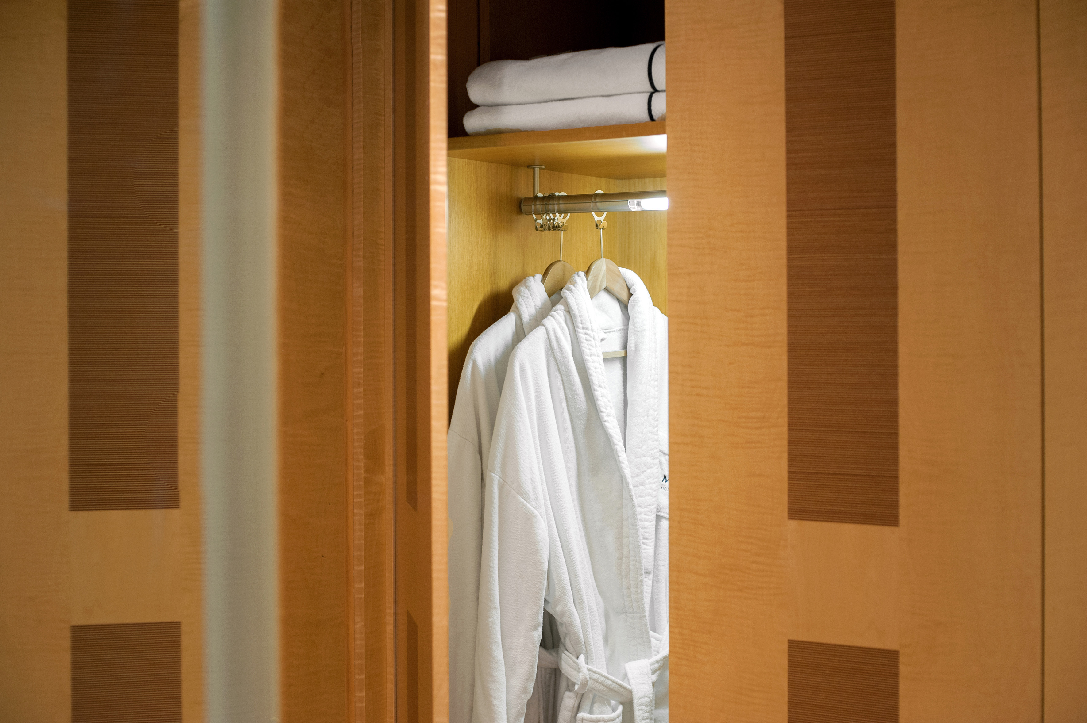Hotel closet with white terry cloth bathrobes and fresh towels.