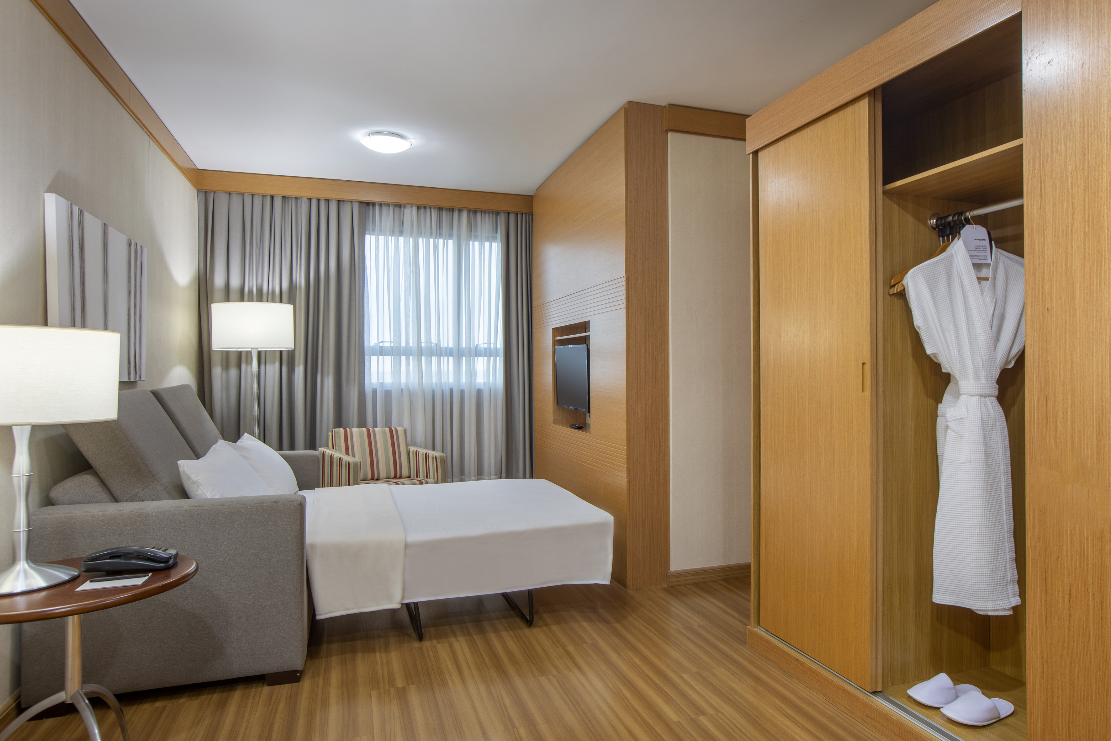 Hotel suite with pull-out sofa bed, wooden wardrobe, TV, and bathrobe.