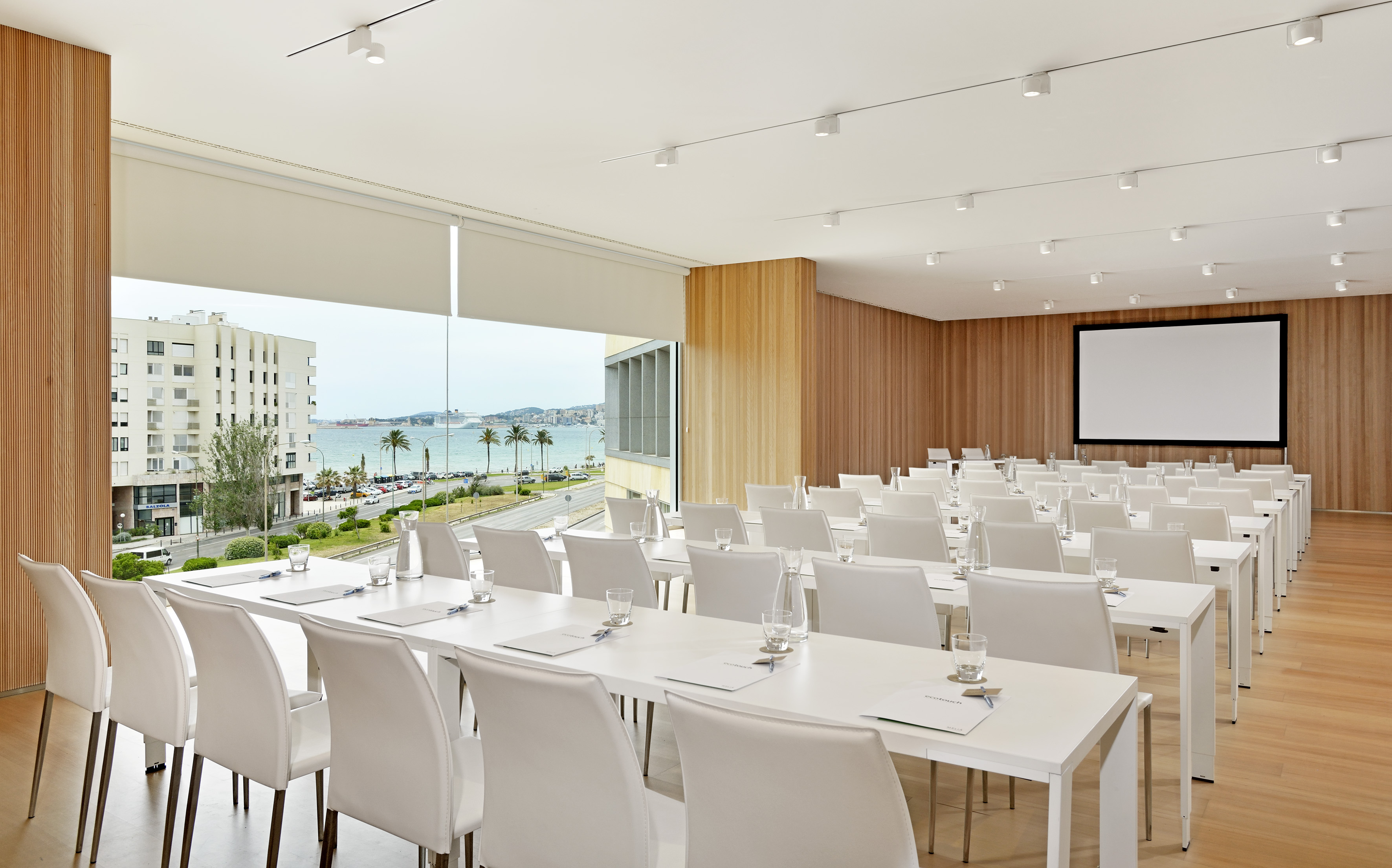 Modern event venue with sea view, white tables, and projector screen.