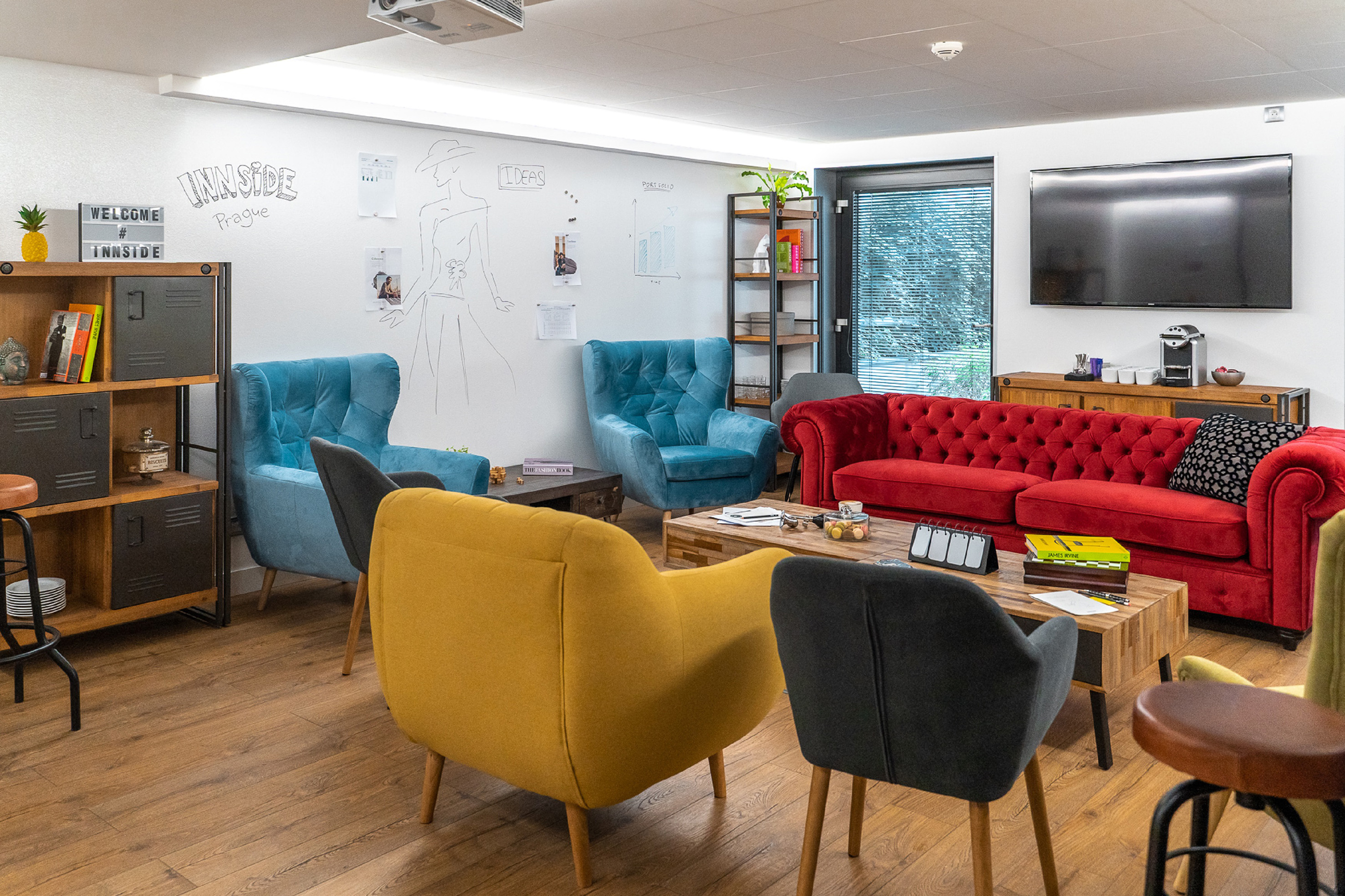 INNSIDE Prague lounge: colorful modern seating, whiteboard, and TV.